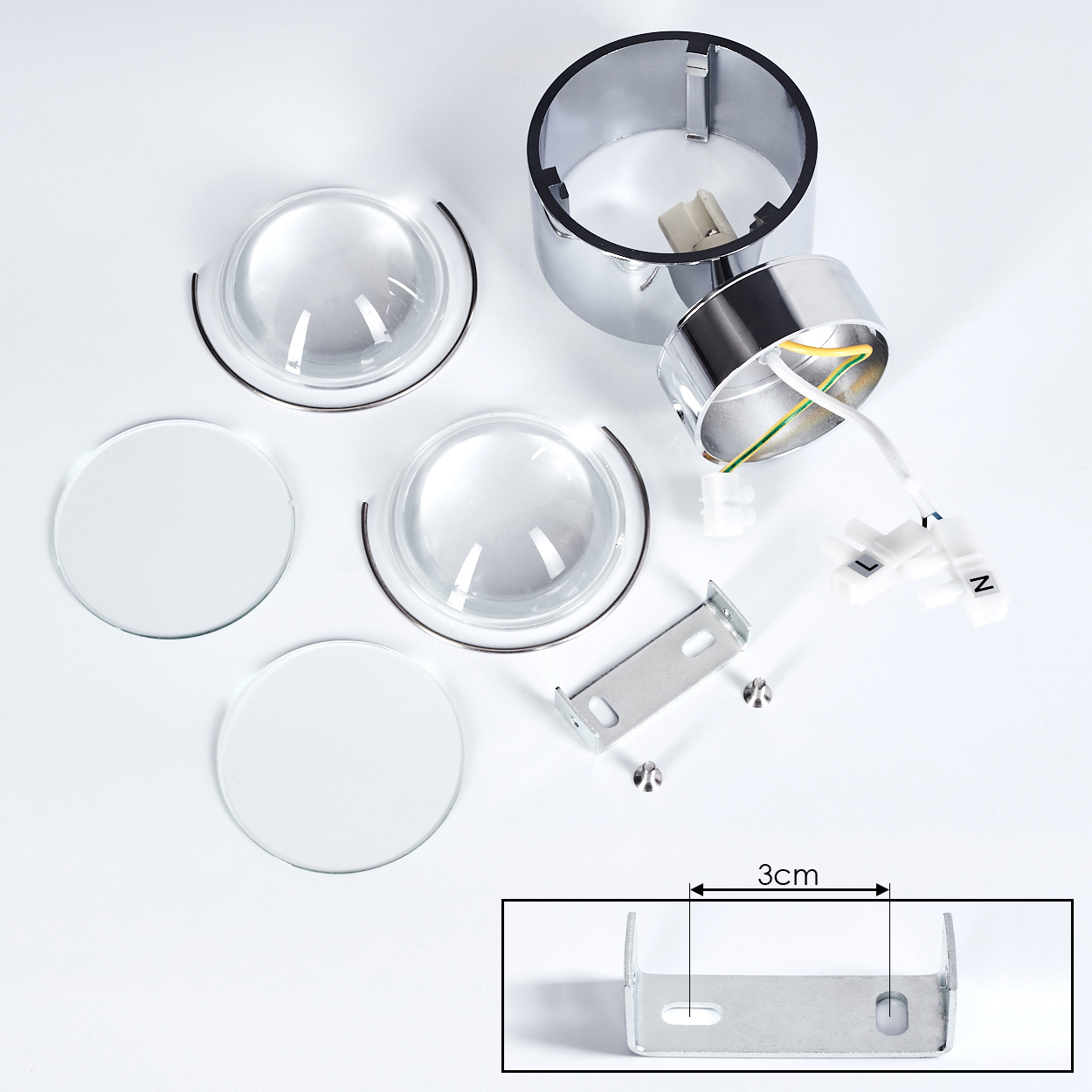 Zerlegte Lampenteile auf weißem Hintergrund: Chromringe, Linsen, Glasscheiben, Schrauben, Verkabelung und eine Halterung. Eine 3 cm Messung gezeigt.