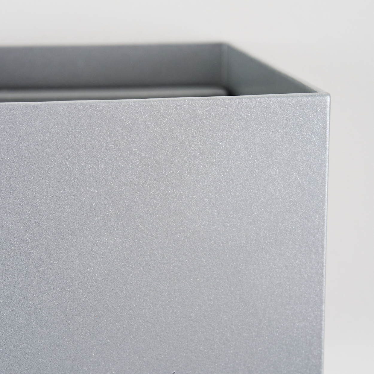 Nahaufnahme einer silbernen Box. Die Box ist metallisch und reflektiert Licht. Der Hintergrund ist eine schlichte weiße Wand.