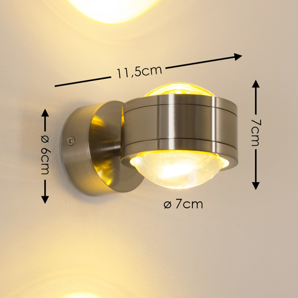 Eine metallische Wandlampe mit rundem Sockel und zylindrischem Kopf. Messungen sind beschriftet. Die Lampe ist an einer hellen Wand montiert.