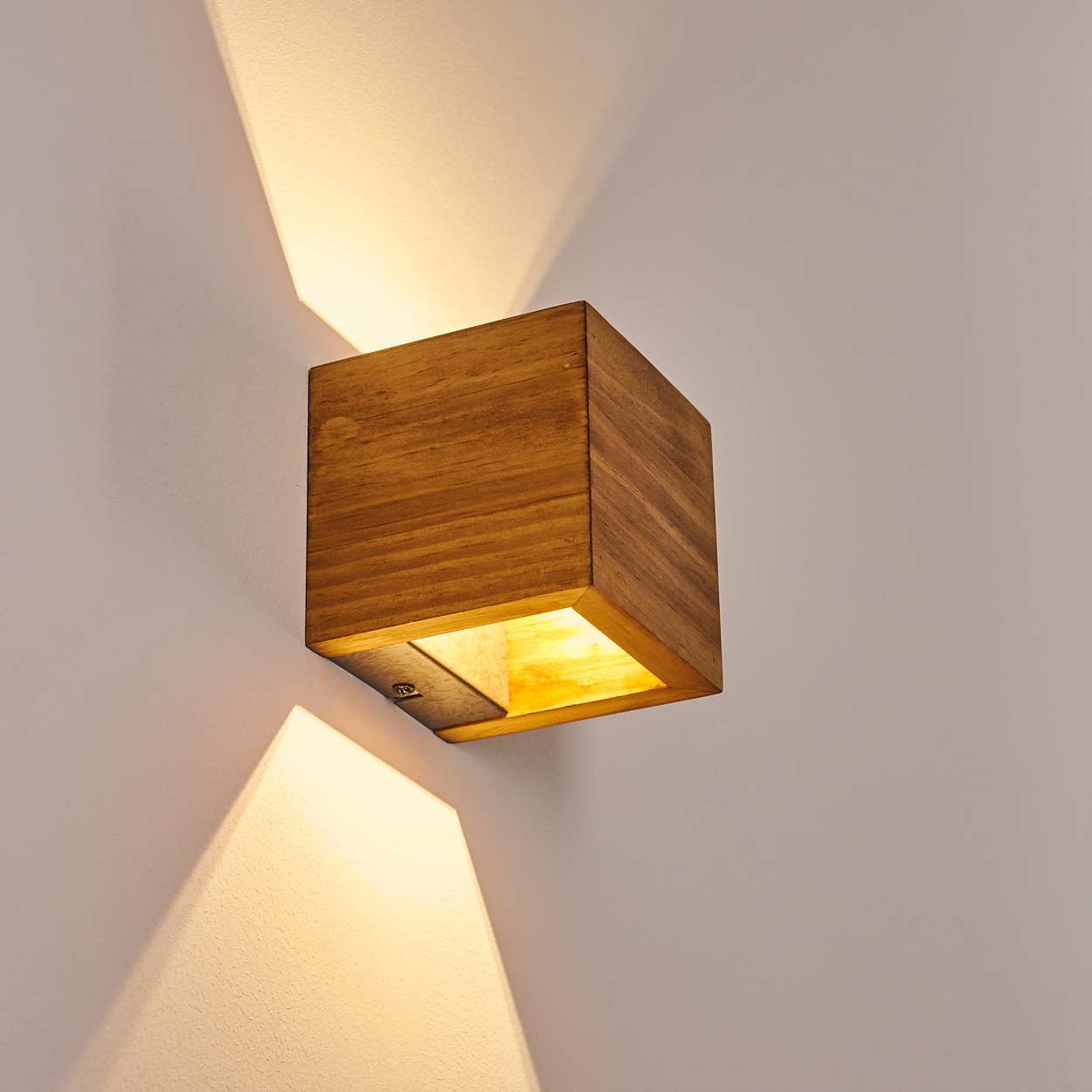 Holzwürfel-Wandlampe, die Licht nach oben und unten abstrahlt. Das Licht erzeugt dreieckige Schatten an der weißen Wand.