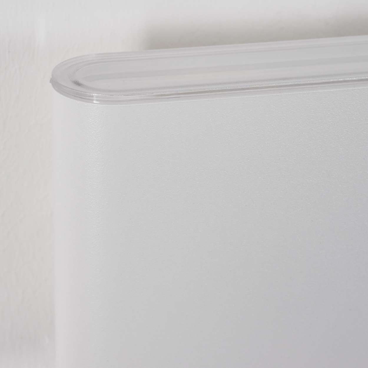 Nahaufnahme eines weißen Behälters mit transparentem Deckel. Der Hintergrund ist eine weiße Wand.