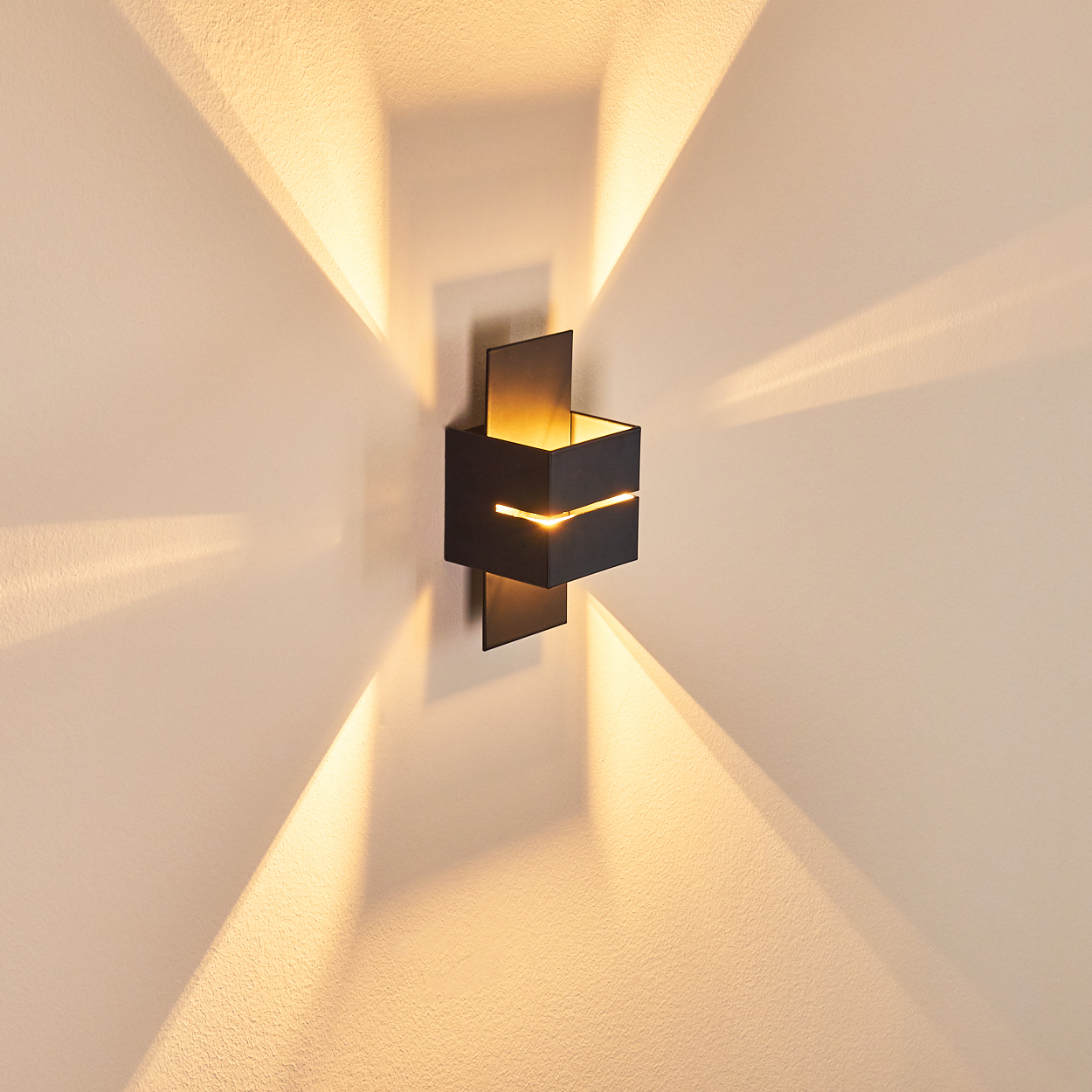 Eine moderne schwarze Wandleuchte mit warmem Licht. Das Licht erzeugt sternförmige Muster auf der hellbeigen Wand.
