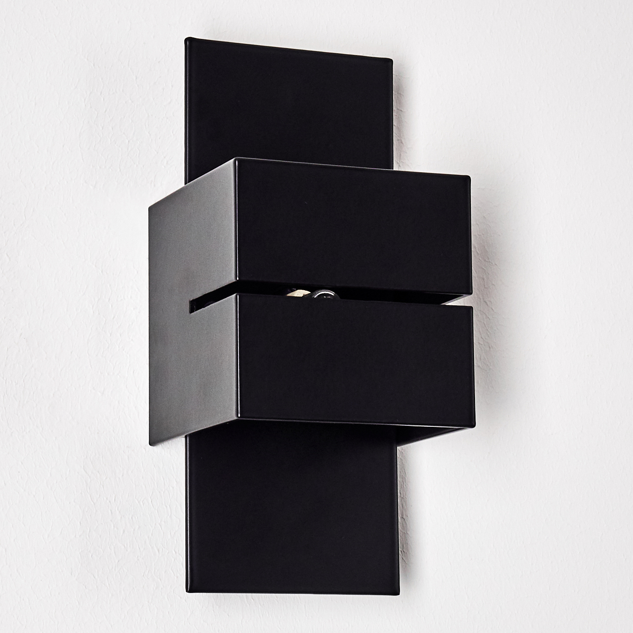 Eine moderne schwarze Wandleuchte ist an einer weißen Wand montiert. Die Lampe hat einen rechteckigen Sockel mit einem geschichteten, kastenförmigen Design.