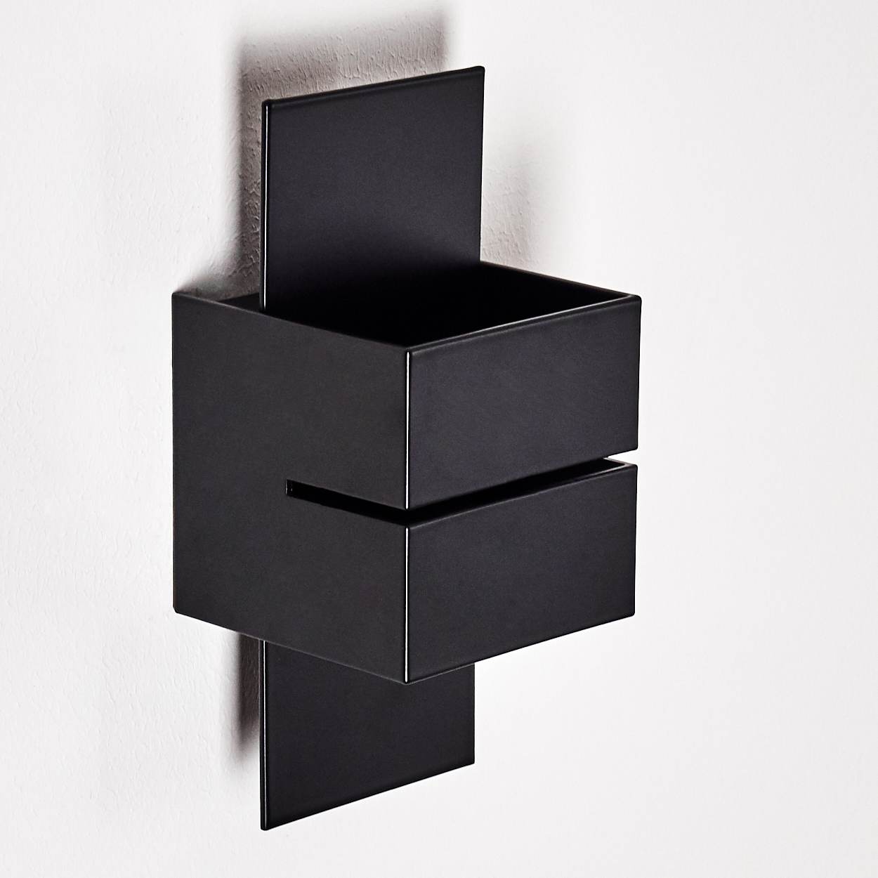 Ein modernes, schwarz an der Wand montiertes Regal mit geometrischem Design, drei Boxen und einem vertikalen Element, an einer weißen Wand befestigt.