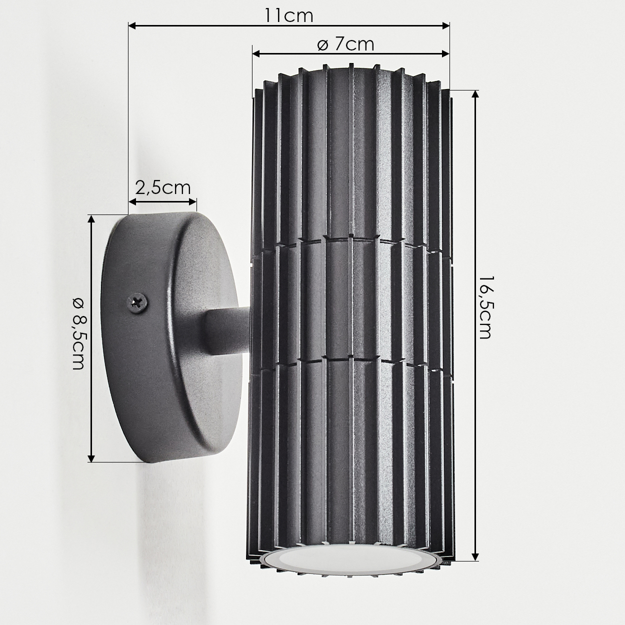 Dunkelgraue Wandleuchte mit Maßangaben. Die Lampe ist zylindrisch mit vertikalen Rippen. An einer Wand mit rundem Sockel befestigt.