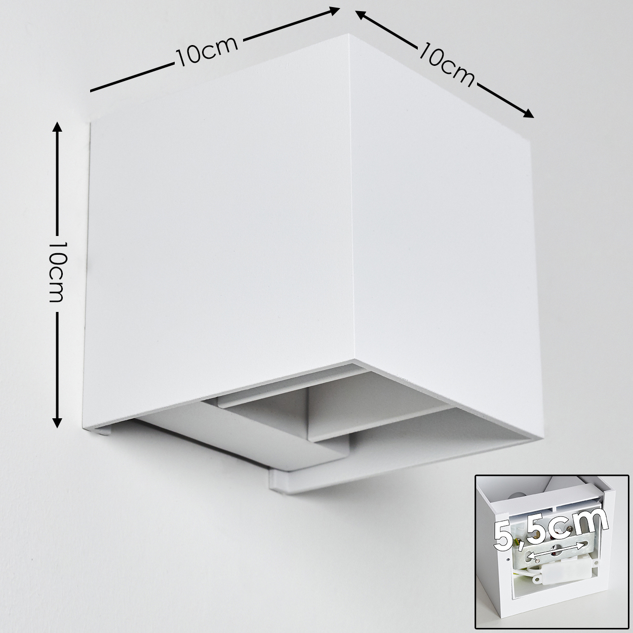 Eine weiße, würfelförmige Wandleuchte ist an einer weißen Wand befestigt. Abmessungen sind beschriftet: 10cm x 10cm. Ein kleinerer Einsatz zeigt die innere Struktur.