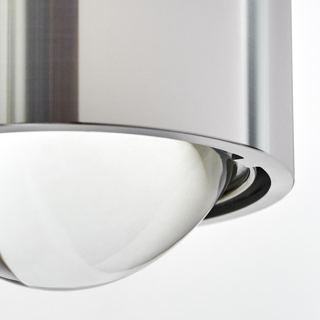 Nahaufnahme eines glänzenden Metallobjekts mit gewölbter, reflektierender Oberfläche, möglicherweise Teil einer Leuchte, vor weißem Hintergrund.