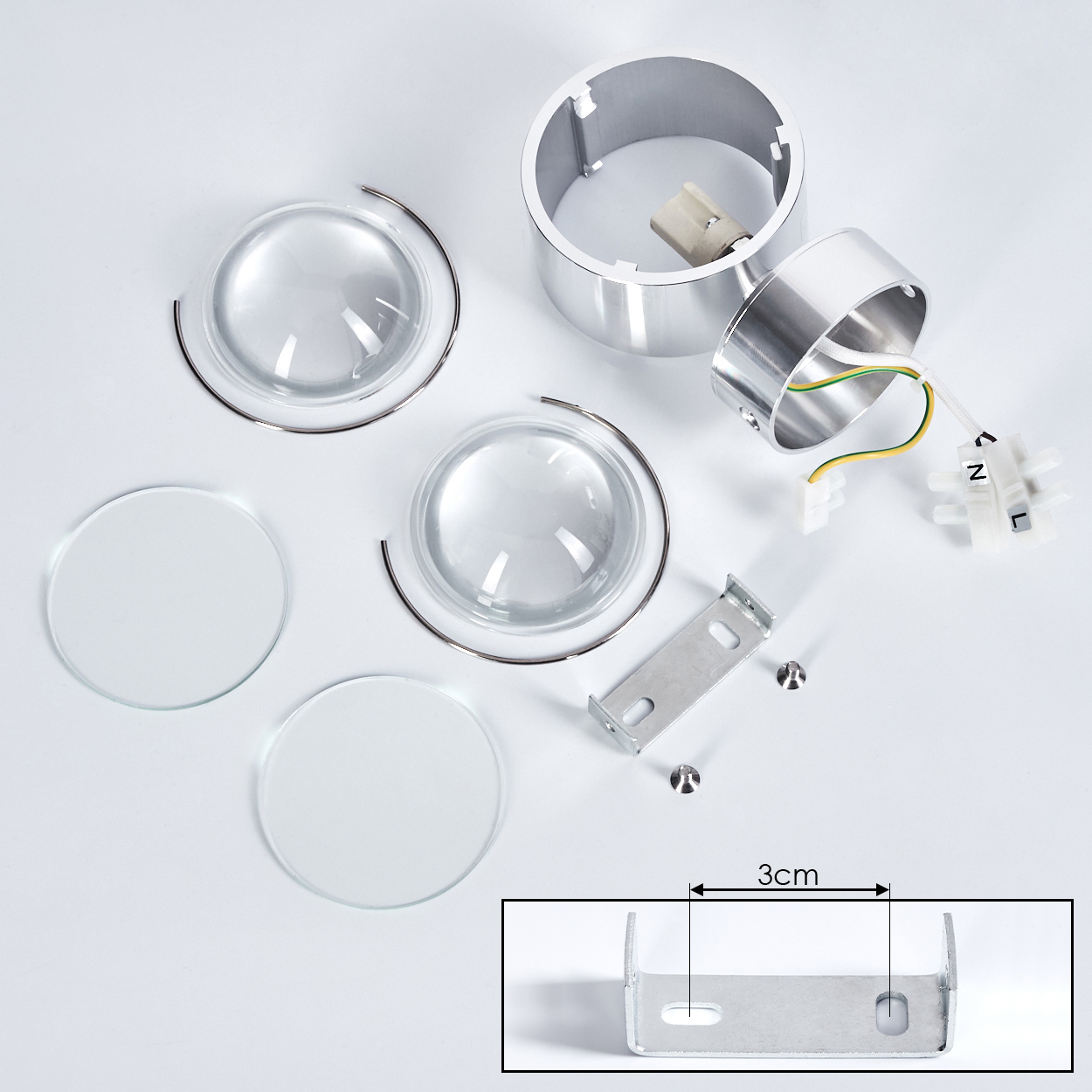 Zerlegte Leuchtenkomponenten auf Weiß. Enthält Linsen, Metallringe, eine Halterung und elektrische Teile. Ein 3-cm-Diagramm ist enthalten.