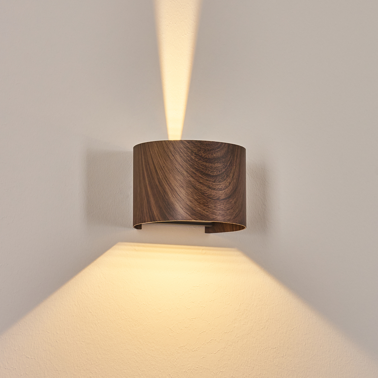 Eine hölzerne Wandleuchte ist an einer hellbeige Wand montiert. Die Lampe strahlt Licht nach oben und unten aus.