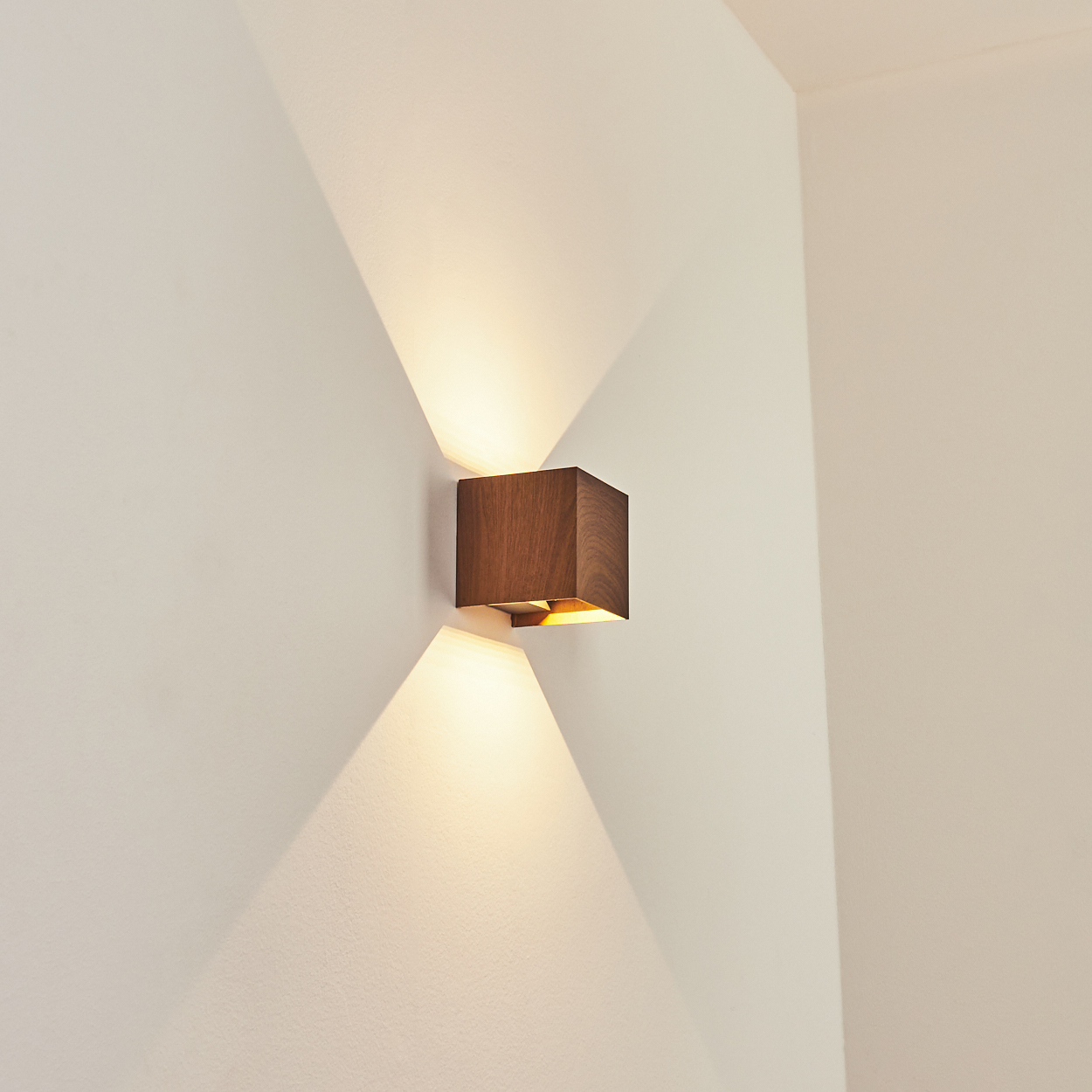 Eine hölzerne Wandleuchte an einer weißen Wand. Die Lampe strahlt Licht nach oben und unten aus.