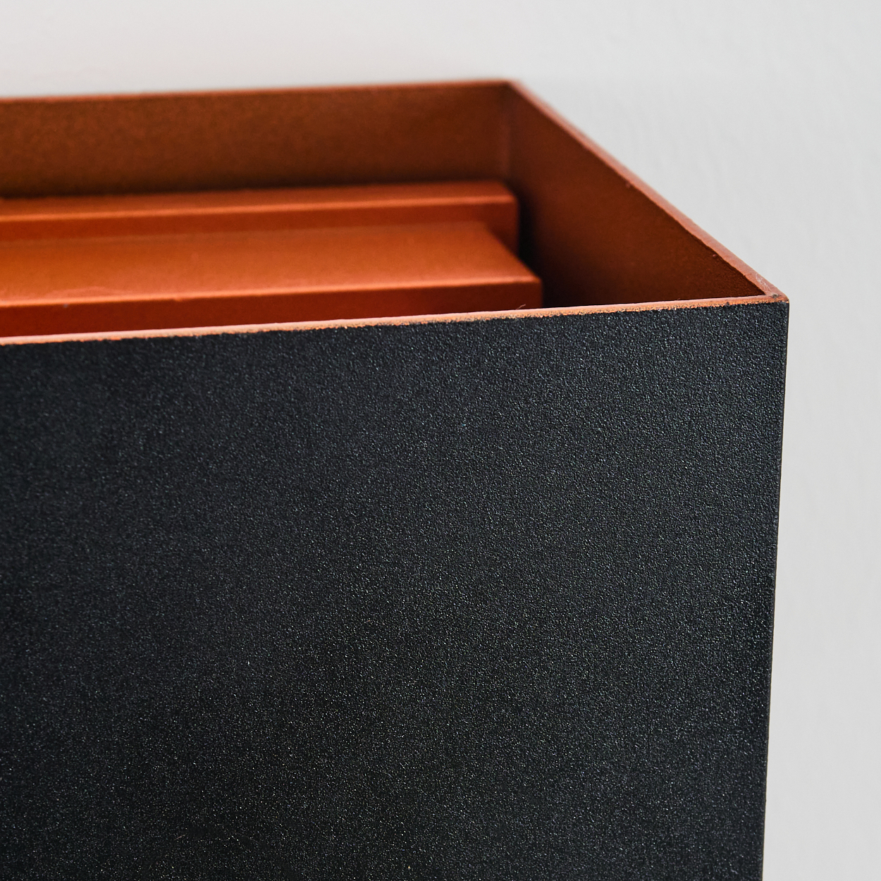 Nahaufnahme einer schwarzen, strukturierten Box mit orangefarbenem Innenraum. Die Box steht vor einem schlichten weißen Hintergrund.