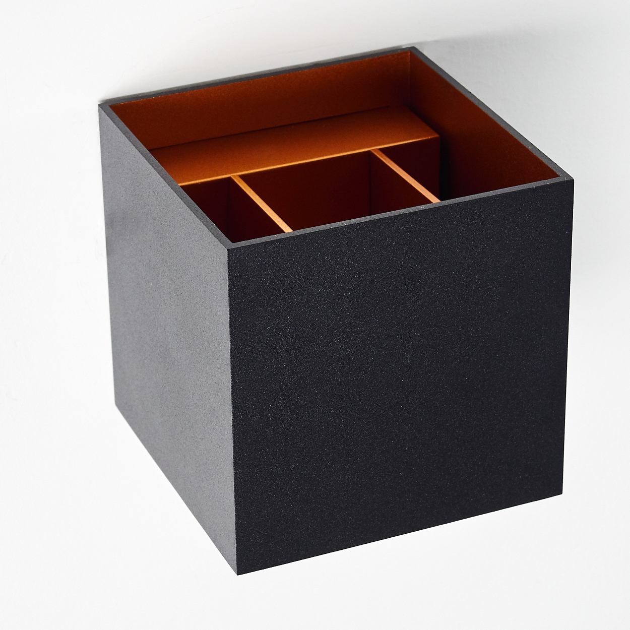 Ein quadratischer, schwarzer Behälter mit orangefarbenem Innenraum und Trennwänden vor weißem Hintergrund.