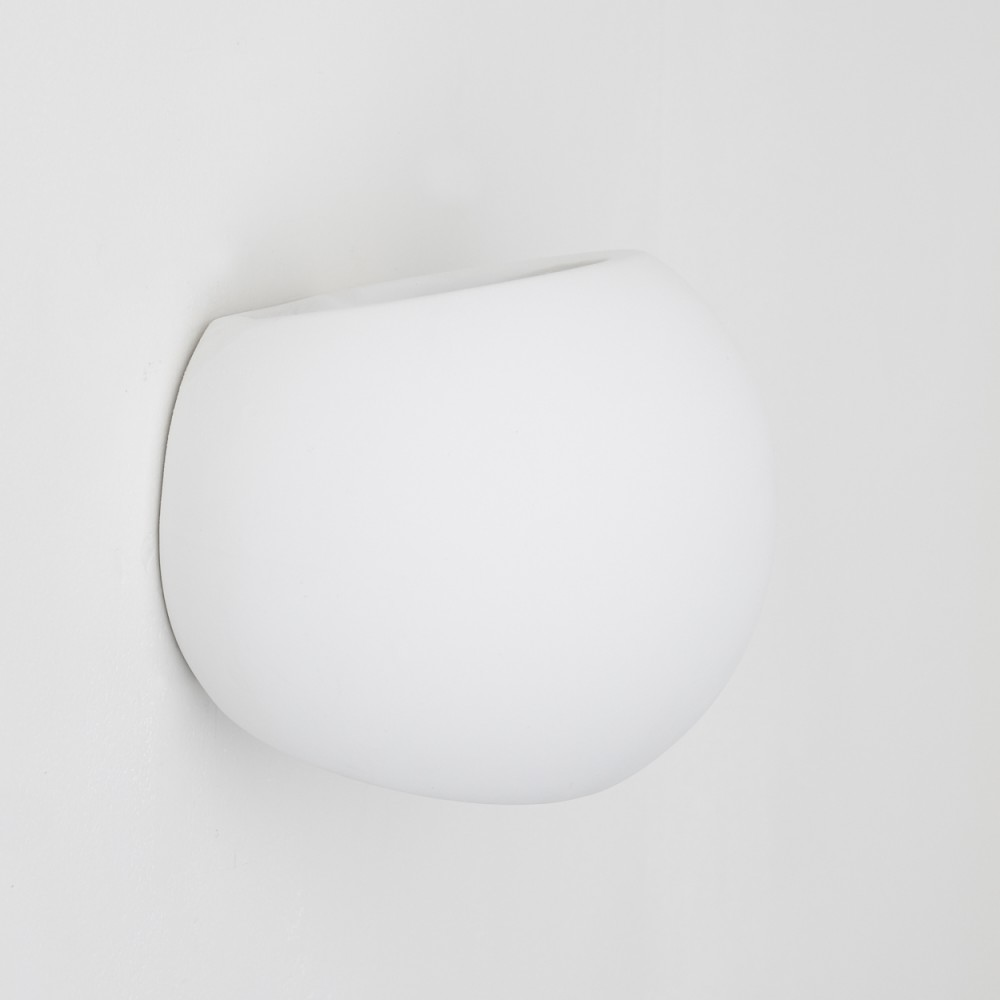 Eine weiße, oval geformte Wandleuchte ist an einer weißen Wand befestigt. Die Lampe hat eine glatte, geschwungene Oberfläche.