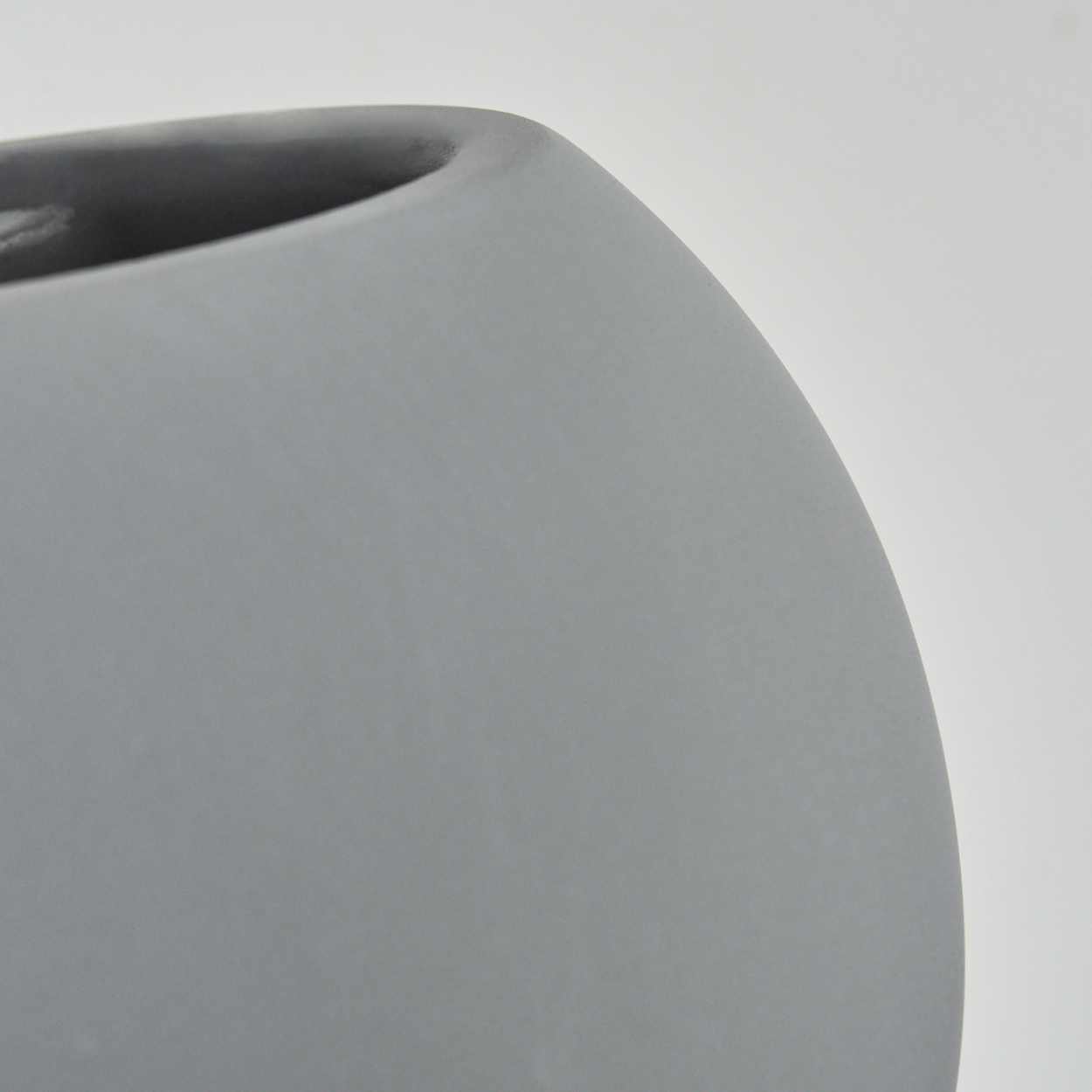 Nahaufnahme einer grauen, oval geformten Keramikvase. Der Hintergrund ist schlicht weiß.