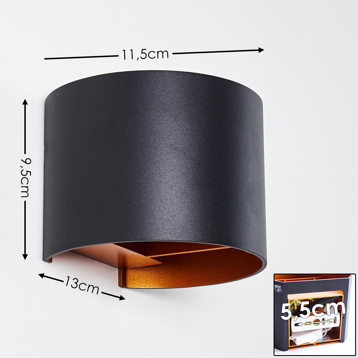 Eine schwarze Wandleuchte mit goldenem Innenraum ist an einer weißen Wand montiert. Abmessungen: 11,5 cm, 9,5 cm und 13 cm. Eine Box ist in der Ecke.
