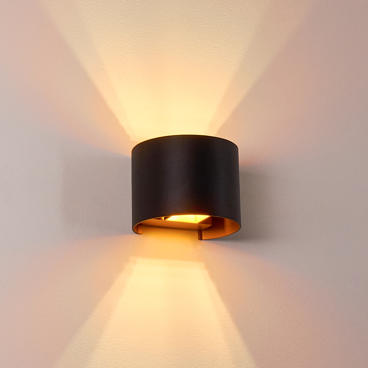 Eine schwarze Wandleuchte mit goldenem Innenraum ist an einer weißen Wand montiert und wirft Licht nach oben und unten.