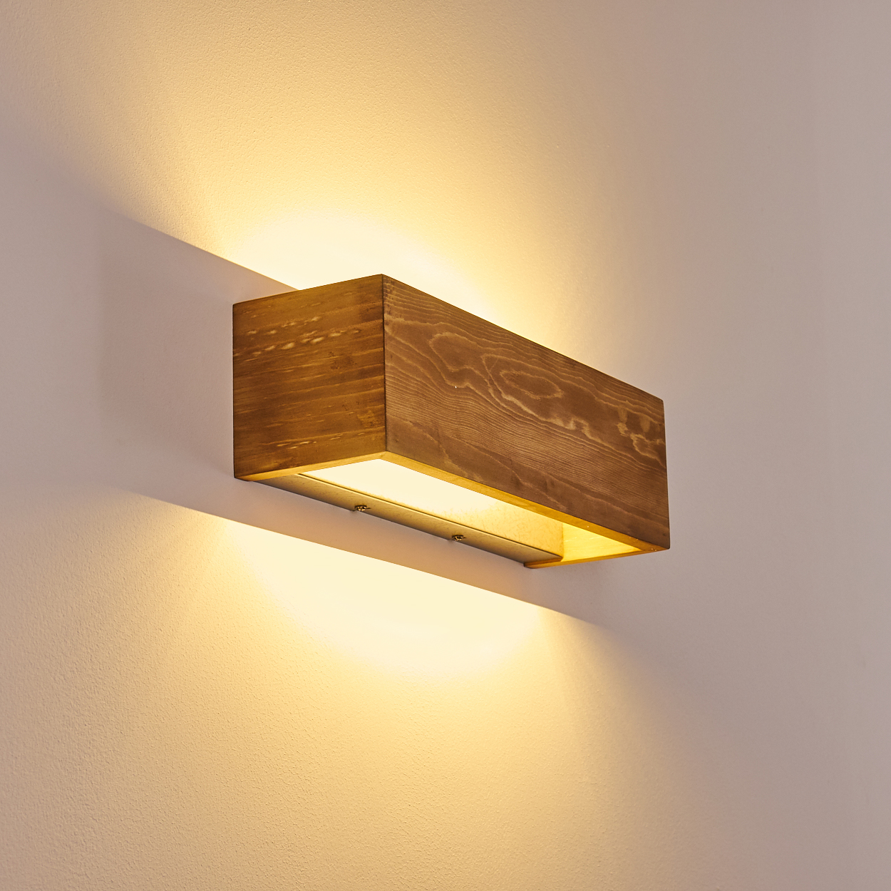 Eine rechteckige Wandleuchte aus Holz strahlt warmes Licht aus. Sie ist an einer strukturierten, hellen Wand angebracht.