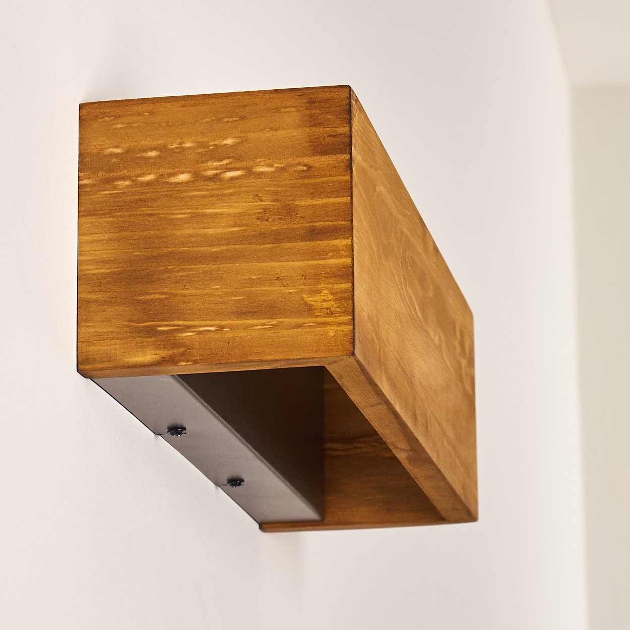 Ein Holzregal ist an einer weißen Wand befestigt. Das Regal ist braun und rechteckig, mit einer dunklen Metallplatte darunter.