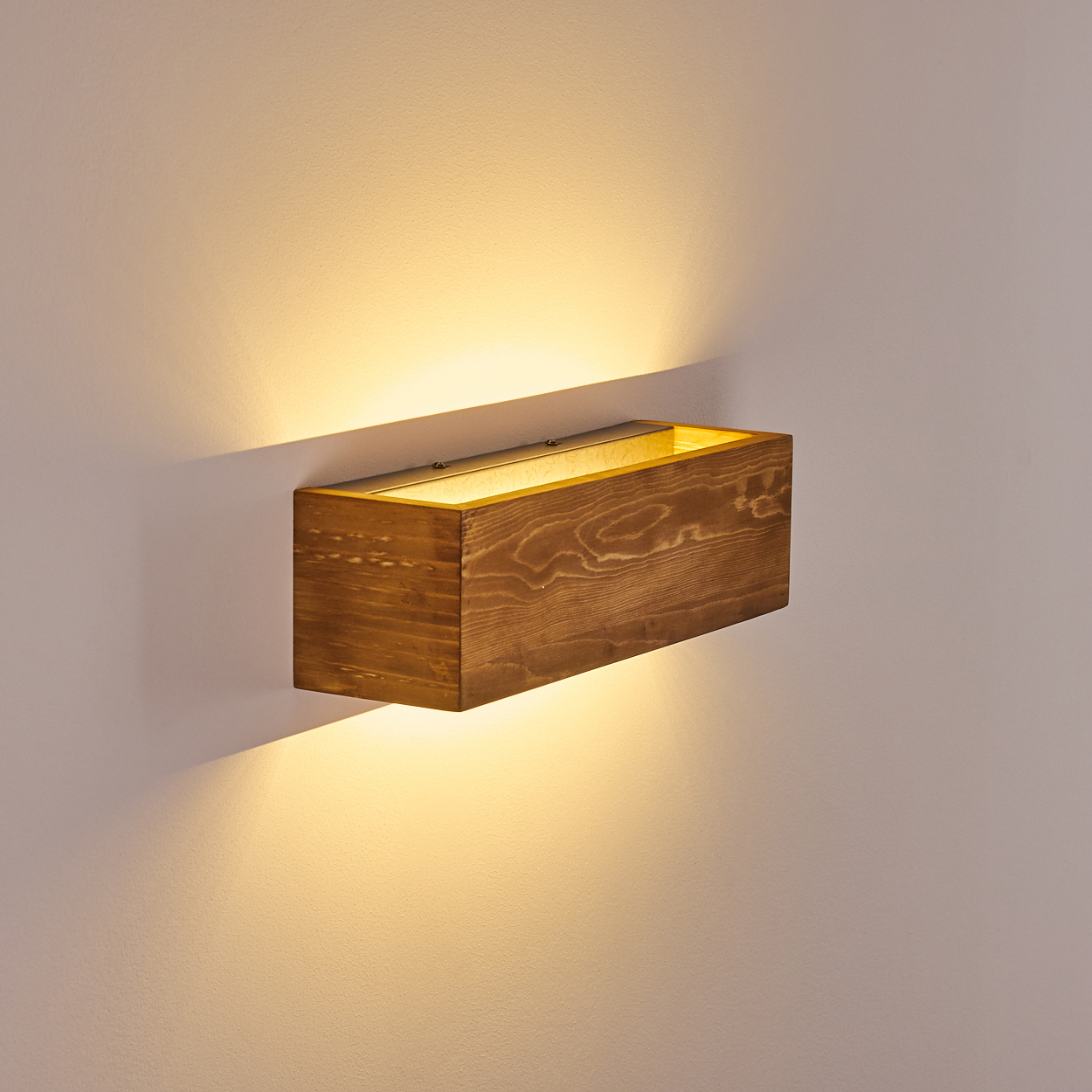 Eine rechteckige Wandleuchte aus Holz mit warmem Licht. Sie ist an einer hellgrauen Wand befestigt. Das Holz hat eine natürliche Maserung.