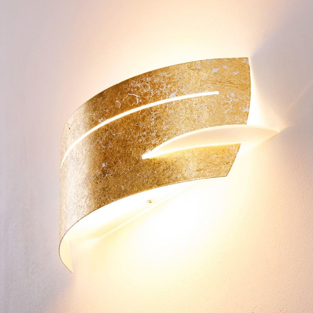 Eine goldene Wandlampe mit geschwungenem Design. Sie wirft ein warmes Licht an die Wand.