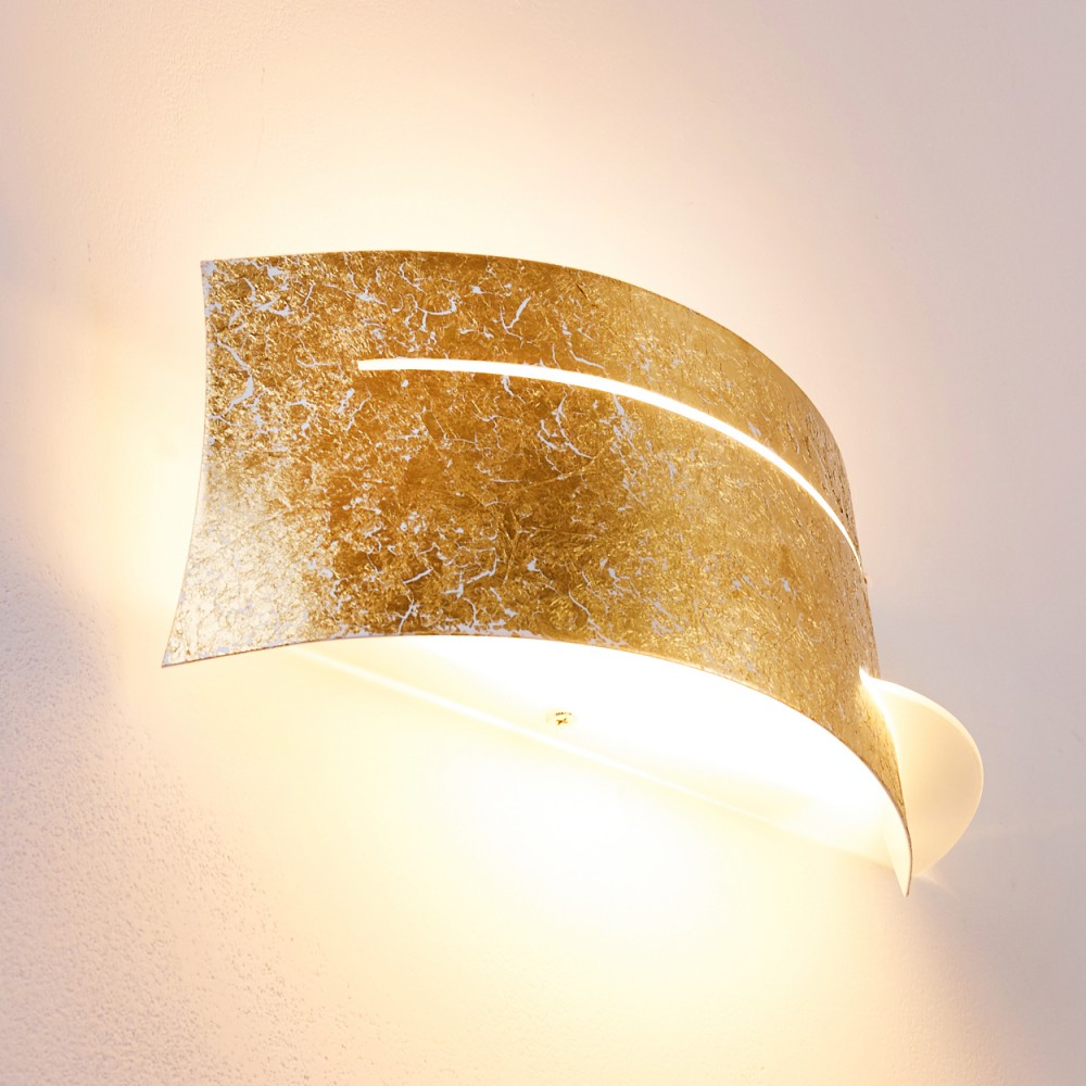 Eine goldene Wandlampe mit geschwungenem Design. Die Lampe hat eine strukturierte Oberfläche und strahlt warmes Licht aus, an einer weißen Wand befestigt.