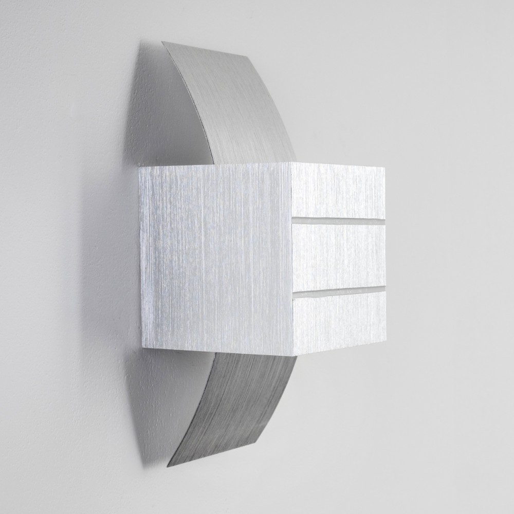 Eine moderne silberne Wandleuchte mit einem rechteckigen Block und gebogenen Metallakzenten, montiert an einer weißen Wand. Sie hat drei horizontale Linien.