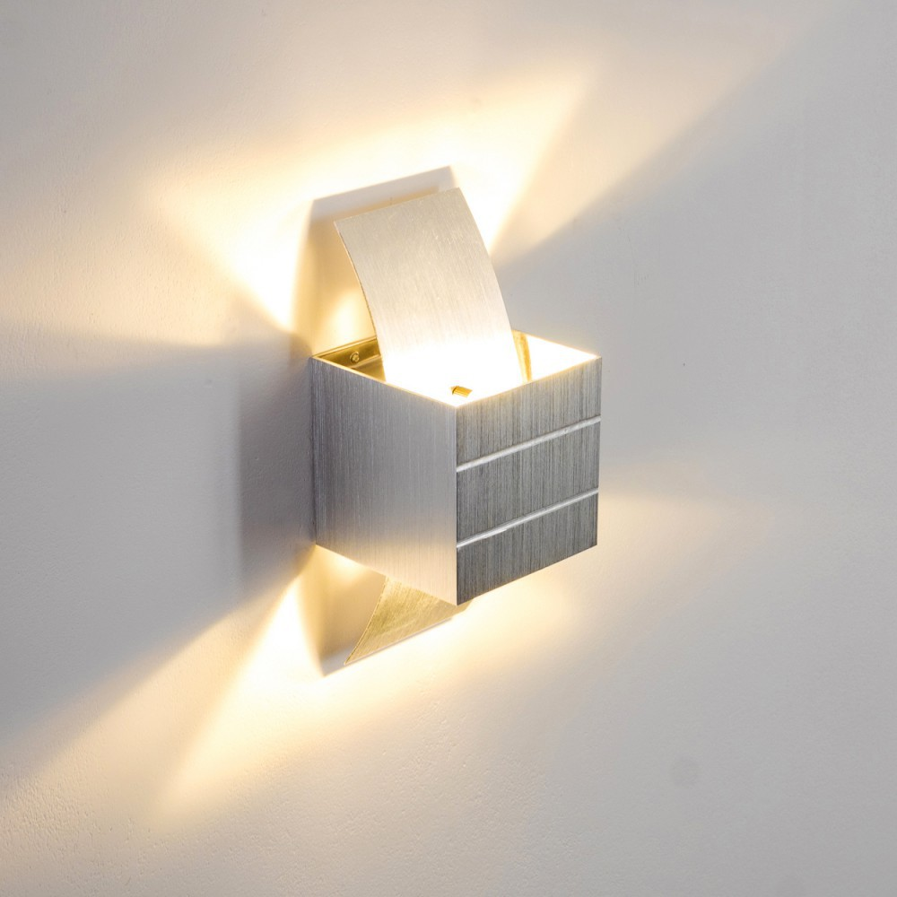 Eine moderne, silberne Wandleuchte ist an einer weißen Wand montiert. Die Lampe strahlt ein warmes Licht aus und schafft eine helle und einladende Atmosphäre.