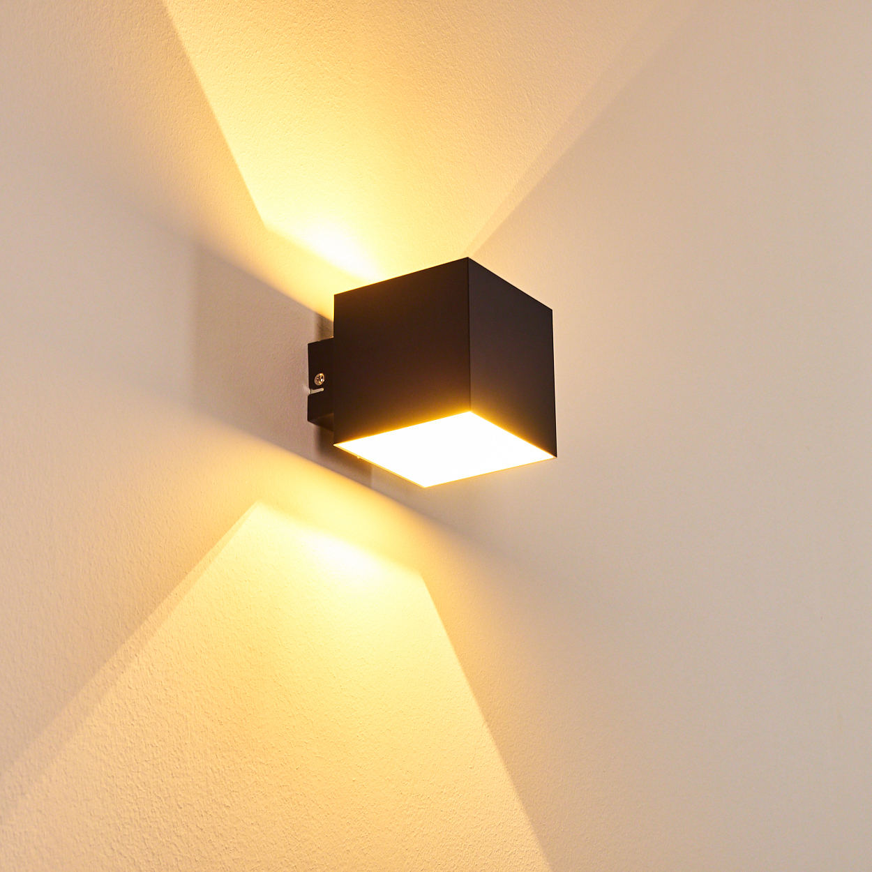 Eine moderne schwarze Wandleuchte strahlt helles Licht auf eine beige Wand. Das Licht erzeugt dreieckige Schatten, die das Design verstärken.