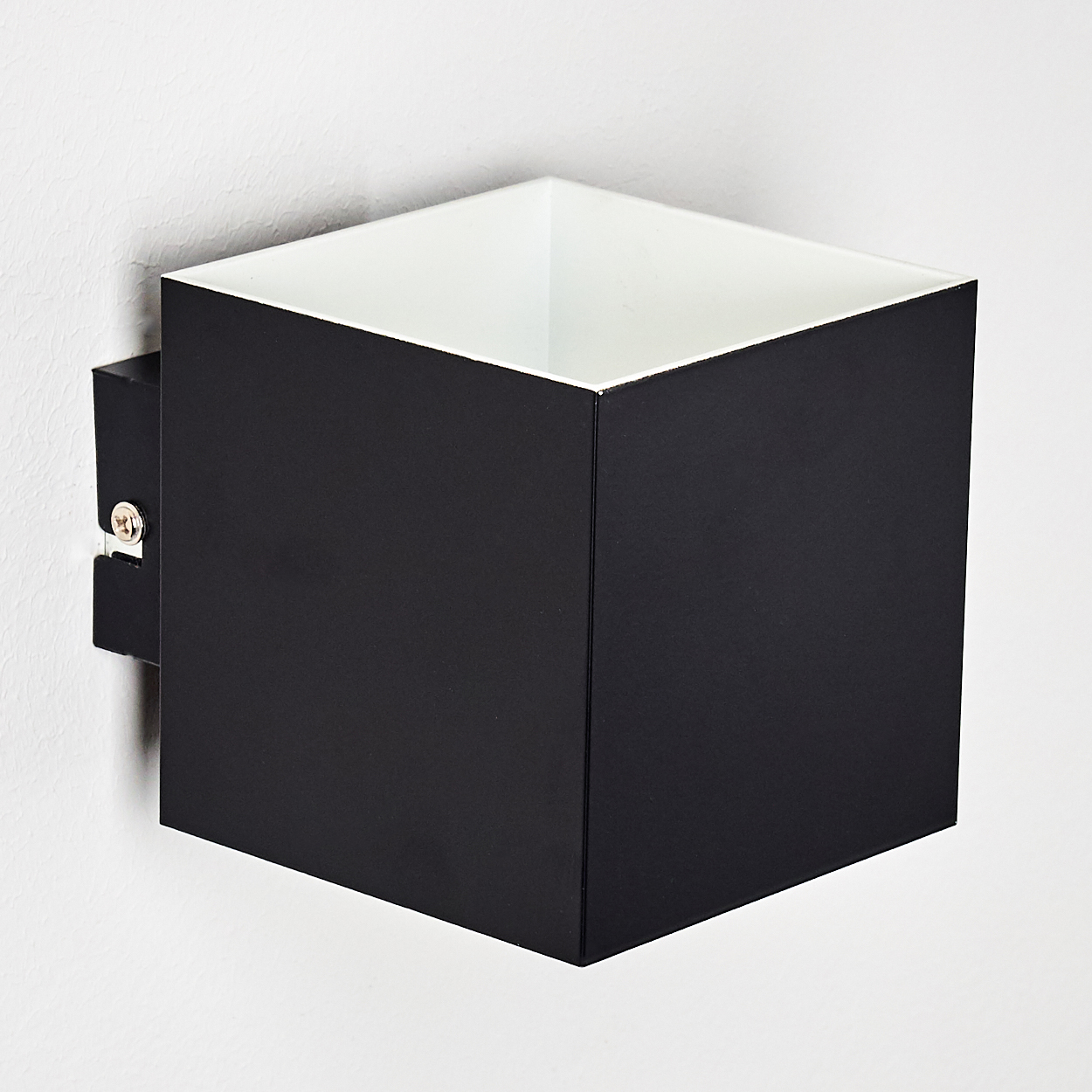 Eine quadratische schwarze Wandleuchte mit weißem Innenraum ist an einer weißen Wand montiert. Eine Metallhalterung hält die Lampe.