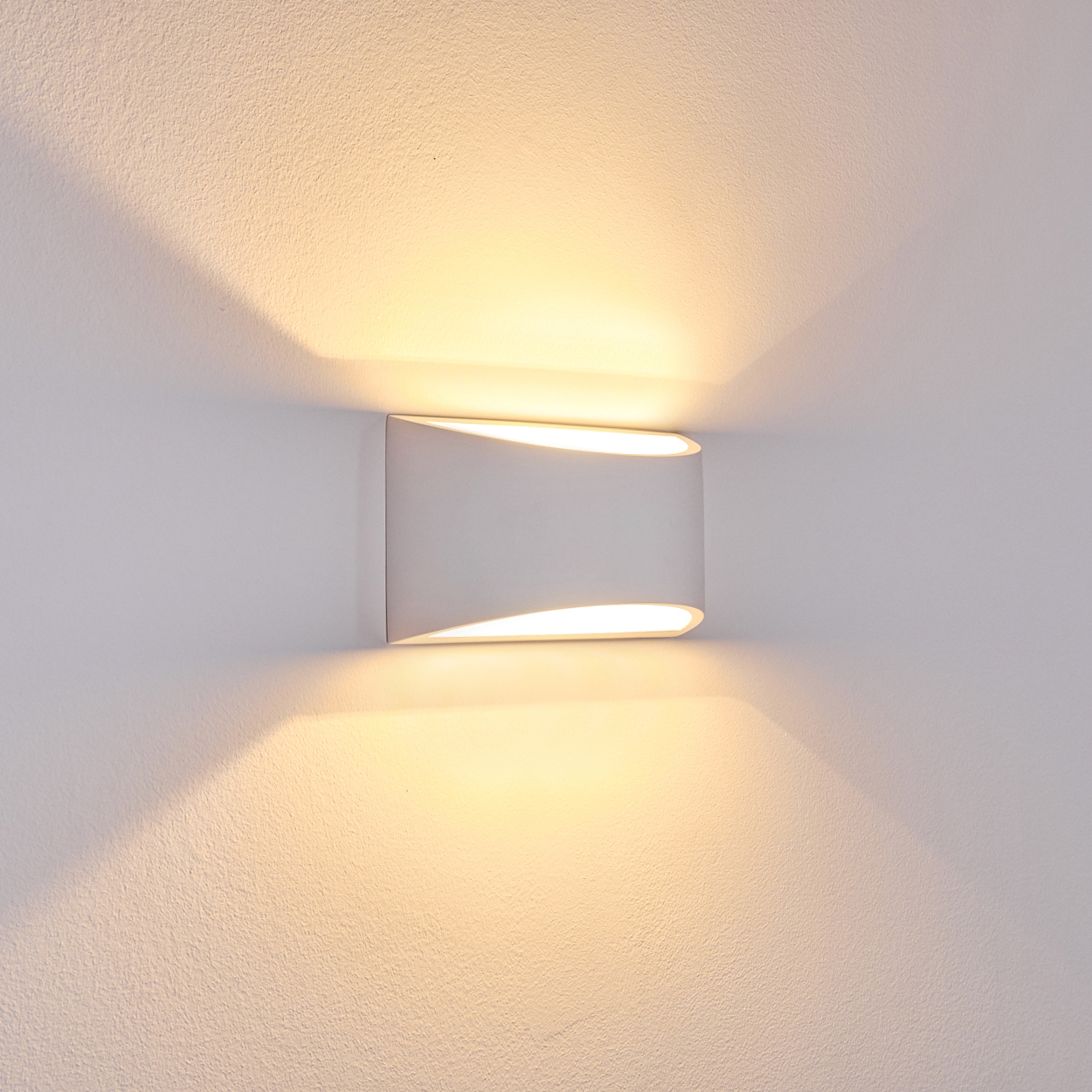 Eine weiße Wandleuchte strahlt Licht nach oben und unten aus und wirft Schatten auf die strukturierte weiße Wand.