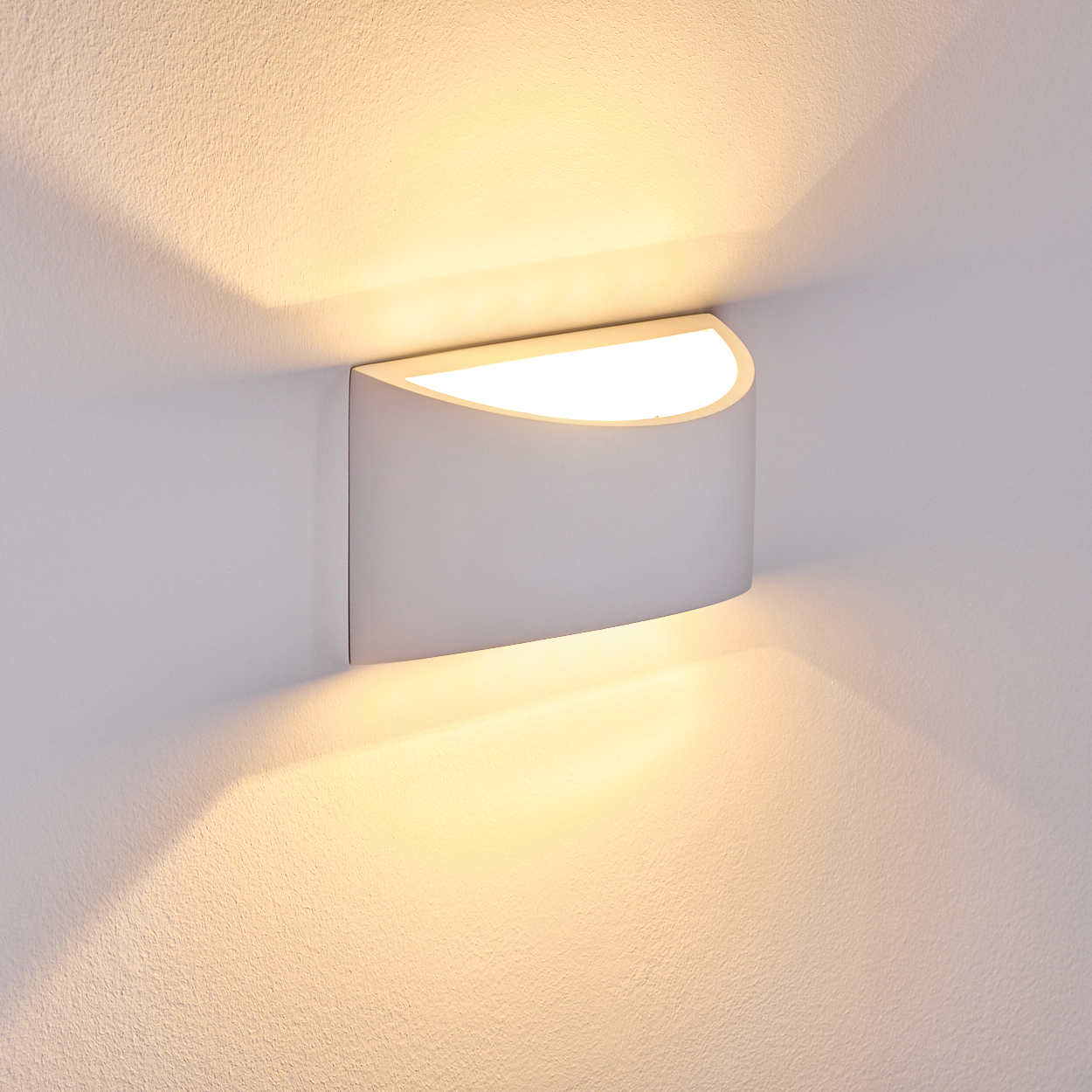 Eine moderne, weiße Wandleuchte mit geschwungenem Design, die warmes Licht auf eine strukturierte weiße Wand wirft.