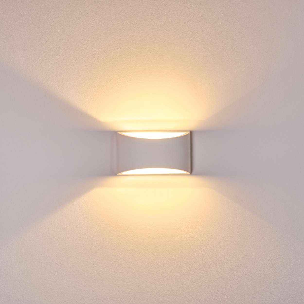 Eine moderne Wandleuchte mit warmem Licht. Die rechteckige Leuchte ist weiß und an einer weißen Wand montiert. Das Licht strahlt nach oben und unten.