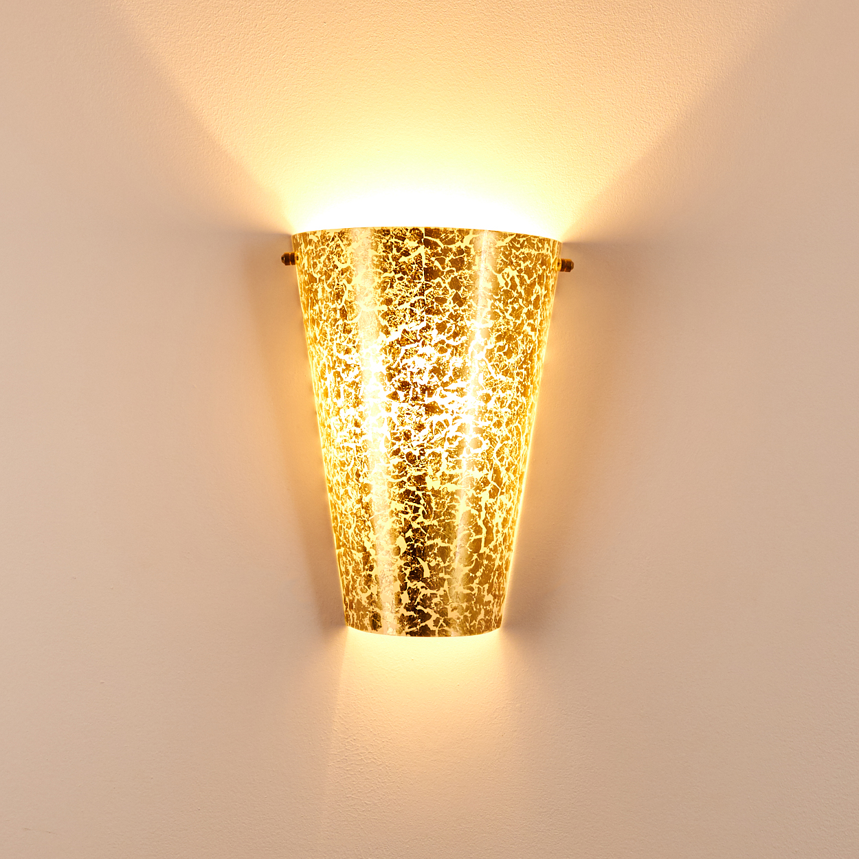 Eine goldene Wandleuchte mit strukturierter Oberfläche, die ein warmes Licht nach oben und unten an eine blasse Wand wirft.