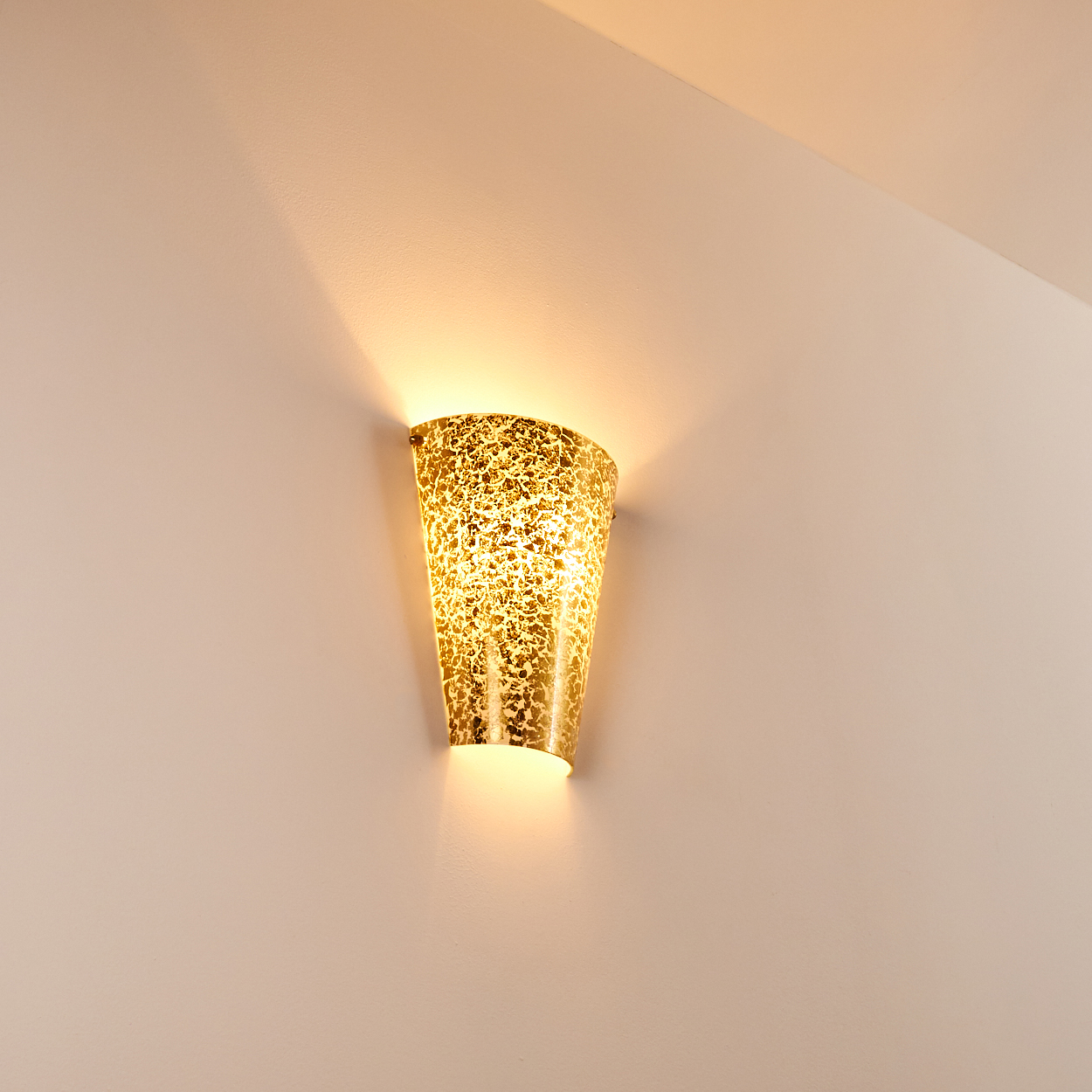 Eine goldene Wandleuchte mit strukturierter Oberfläche ist an einer hellbeige Wand befestigt. Licht scheint nach oben und unten.