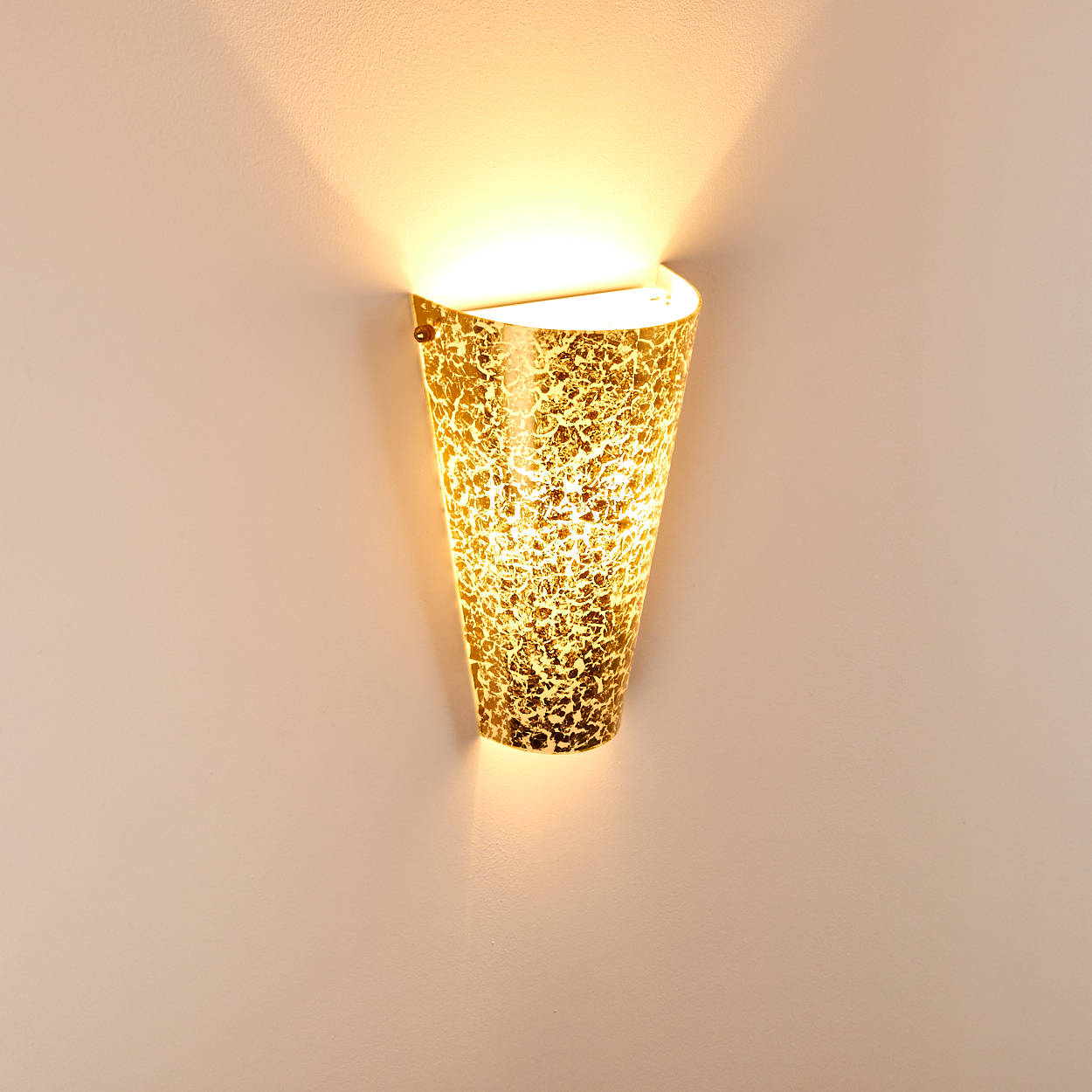 Eine goldene Wandleuchte mit strukturierter Oberfläche strahlt warmes Licht auf eine blasse Wand. Die Leuchte ist konisch geformt.
