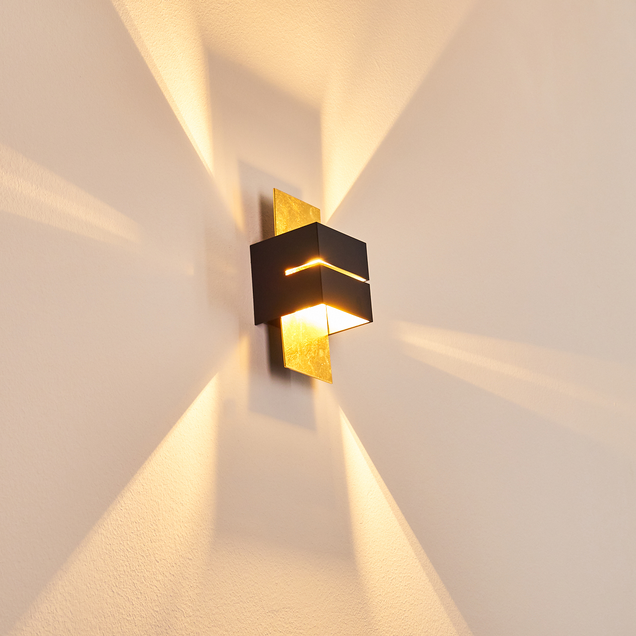 Eine moderne Wandleuchte mit schwarzem und goldenem Design, die das Licht nach oben und unten an eine beige Wand wirft.