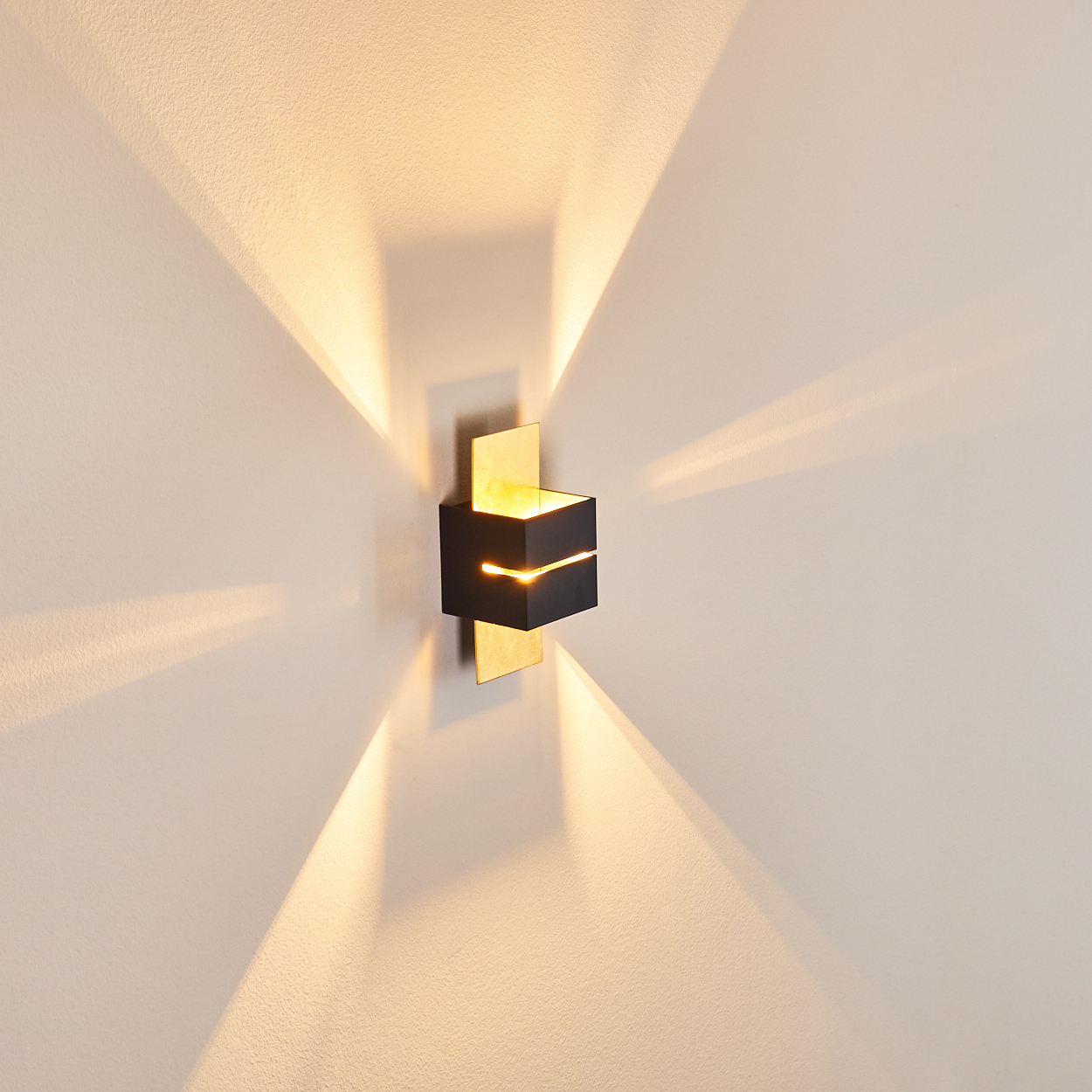 Eine moderne schwarze Wandleuchte mit goldenen Akzenten ist an einer weißen Wand montiert und wirft Licht nach oben und unten.
