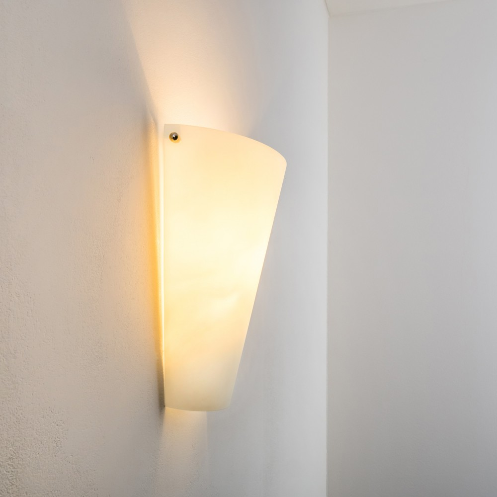 Eine Wandleuchte mit mattiertem Glasschirm ist an einer weißen Wand befestigt. Das Licht ist an und beleuchtet den Schirm und die Wand darum herum.