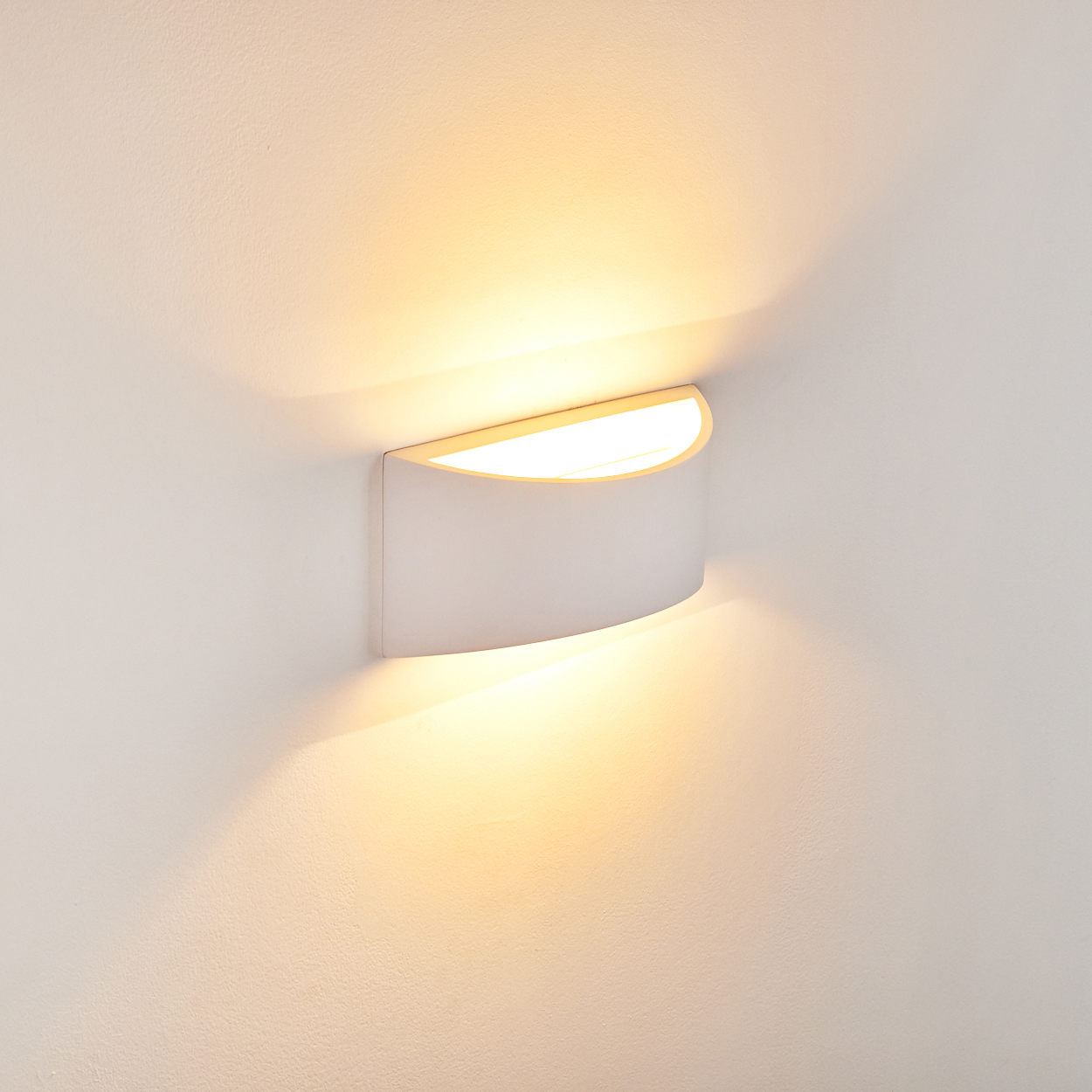 Eine weiße, gebogene Wandleuchte ist an einer weißen Wand montiert und strahlt warmes Licht nach oben und unten aus.