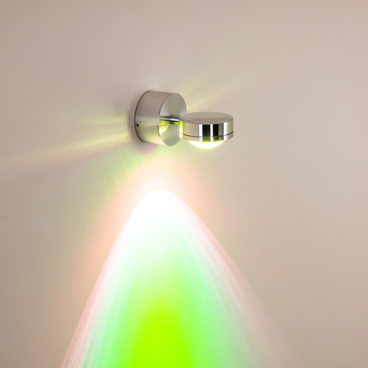 Eine moderne silberne Wandleuchte ist an einer Wand befestigt. Die Lampe strahlt grünes, gelbes und oranges Licht auf die Wand.