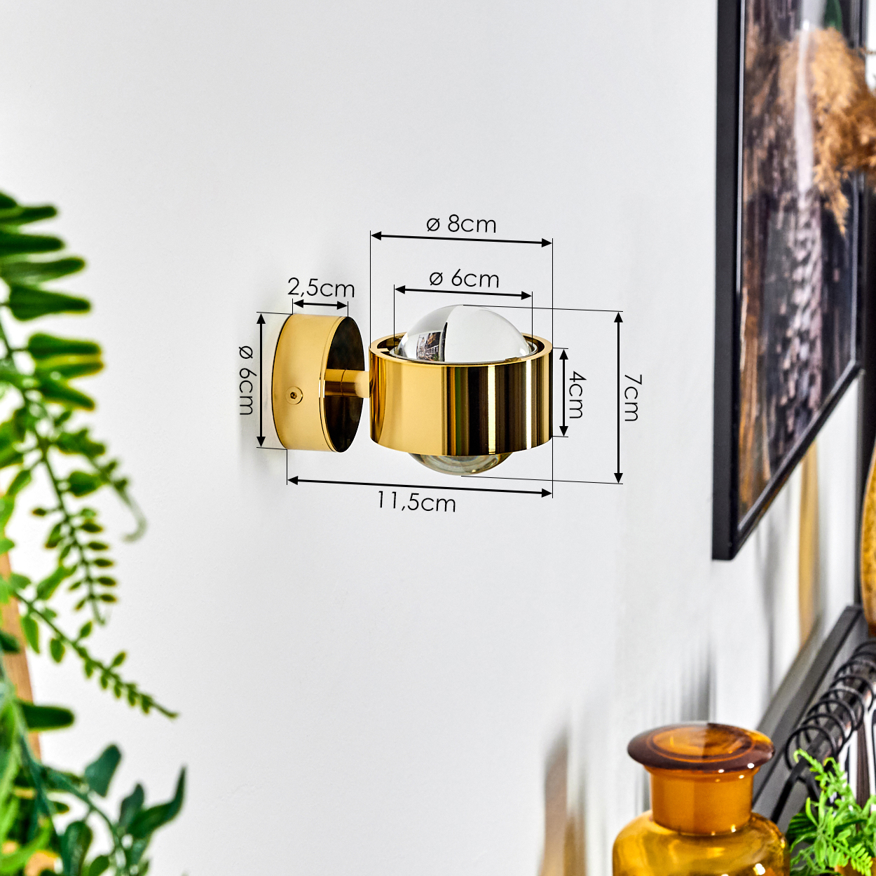 Eine goldene Wandlampe mit Glaskugel. Abmessungen: 6 cm, 8 cm, 2,5 cm, 4 cm, 7 cm und 11,5 cm. Weiße Wand.