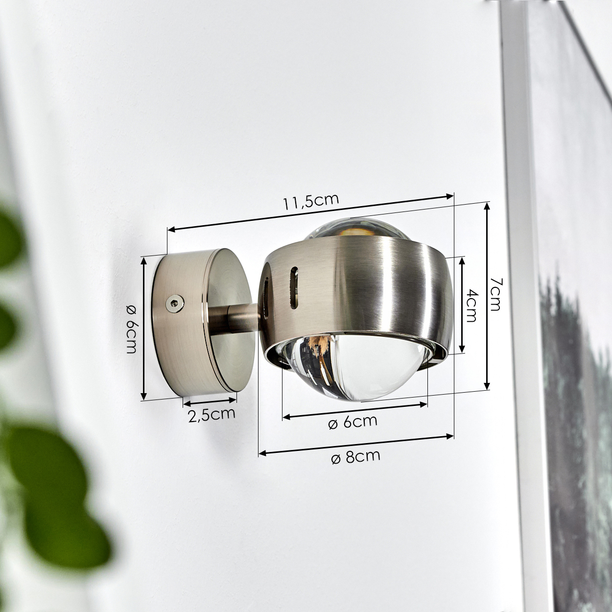 Eine metallische Wandlampe ist an einer weißen Wand befestigt. Abmessungen sind beschriftet: 11,5 cm, 6 cm, 2,5 cm, 7 cm, 4 cm, 6 cm und 8 cm.