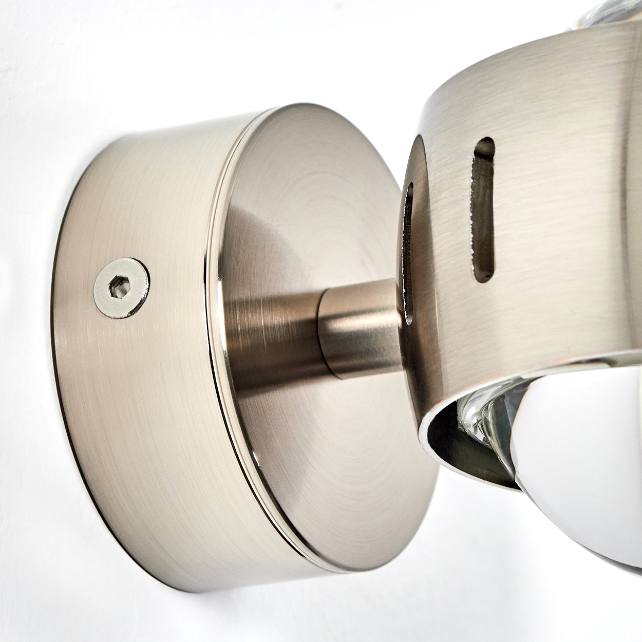Nahaufnahme einer Wandleuchte aus gebürstetem Metall. Sie hat einen kreisförmigen Sockel, einen zylindrischen Arm und eine Leuchte mit Glasabdeckung.