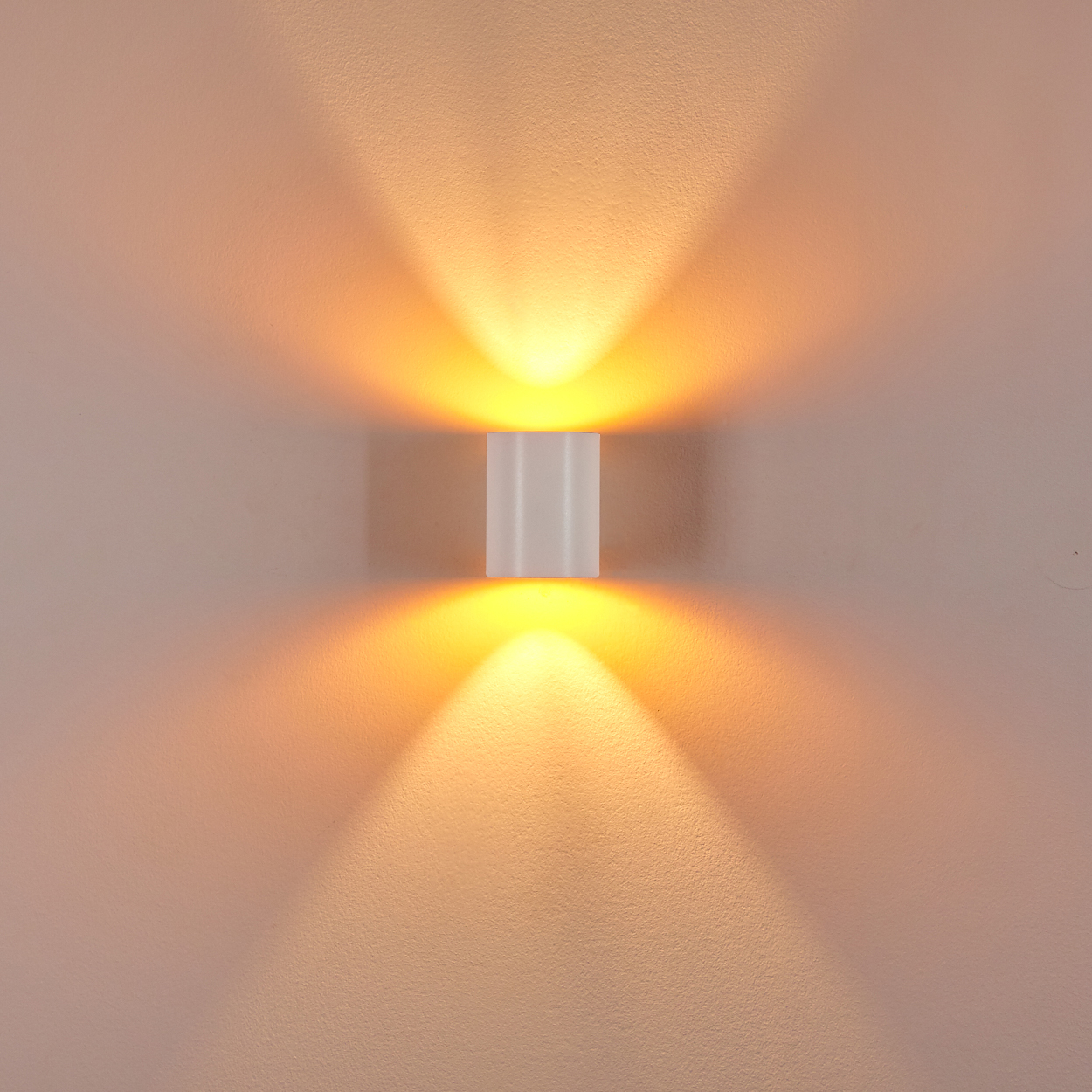 Eine weiße Wandleuchte strahlt warmes Licht nach oben und unten aus. Das Licht erzeugt symmetrische Muster an der Wand.