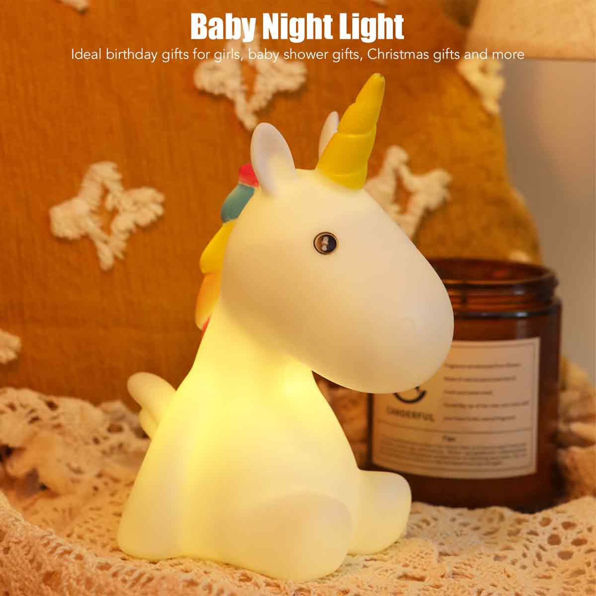 Ein leuchtendes Einhorn-Nachtlicht steht auf einer Spitzendecke. Im Hintergrund befinden sich eine Kerze und ein Kissen. Der Text lautet: Baby Night Light.