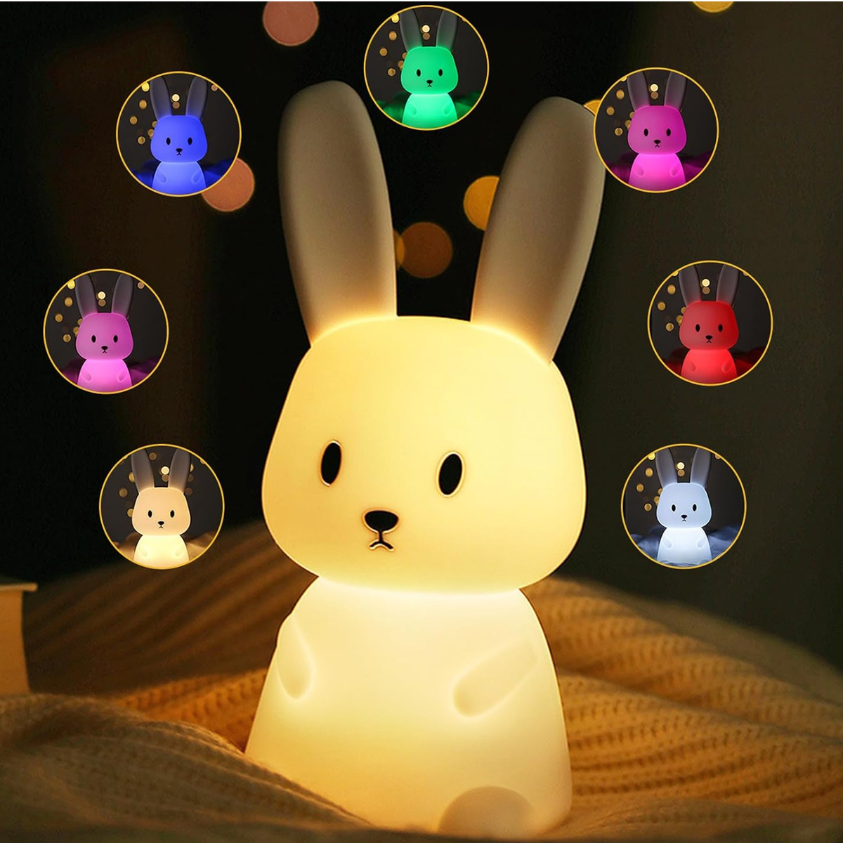 Ein leuchtendes Hasen-Nachtlicht. Kleine bunte Hasenlichter umgeben es. Der Haupt-Hase ist cremefarben und liegt auf einer Decke.