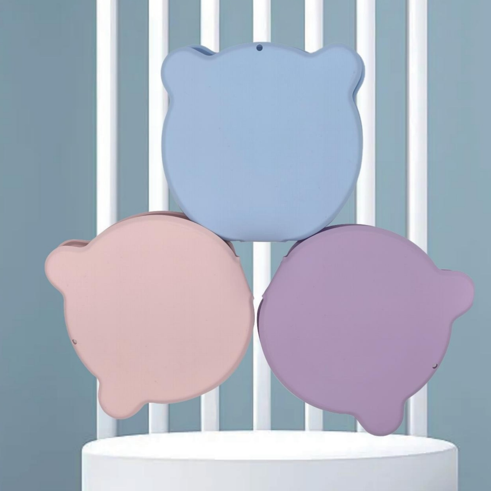 Drei bärenförmige Objekte in Blau, Rosa und Lila sind gestapelt. Sie stehen auf einem weißen Sockel, mit hellblauem Hintergrund.
