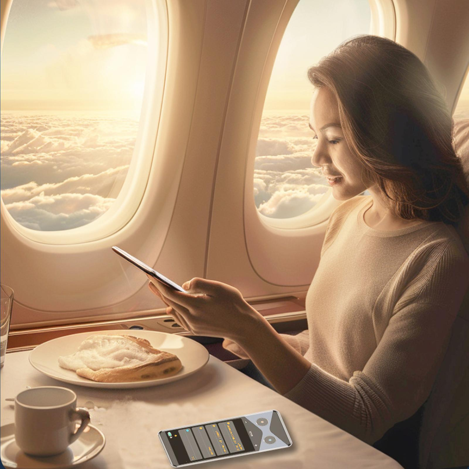 Frau im Flugzeug benutzt Tablet. Wolken sichtbar. Tisch mit Essen und Fernbedienung.