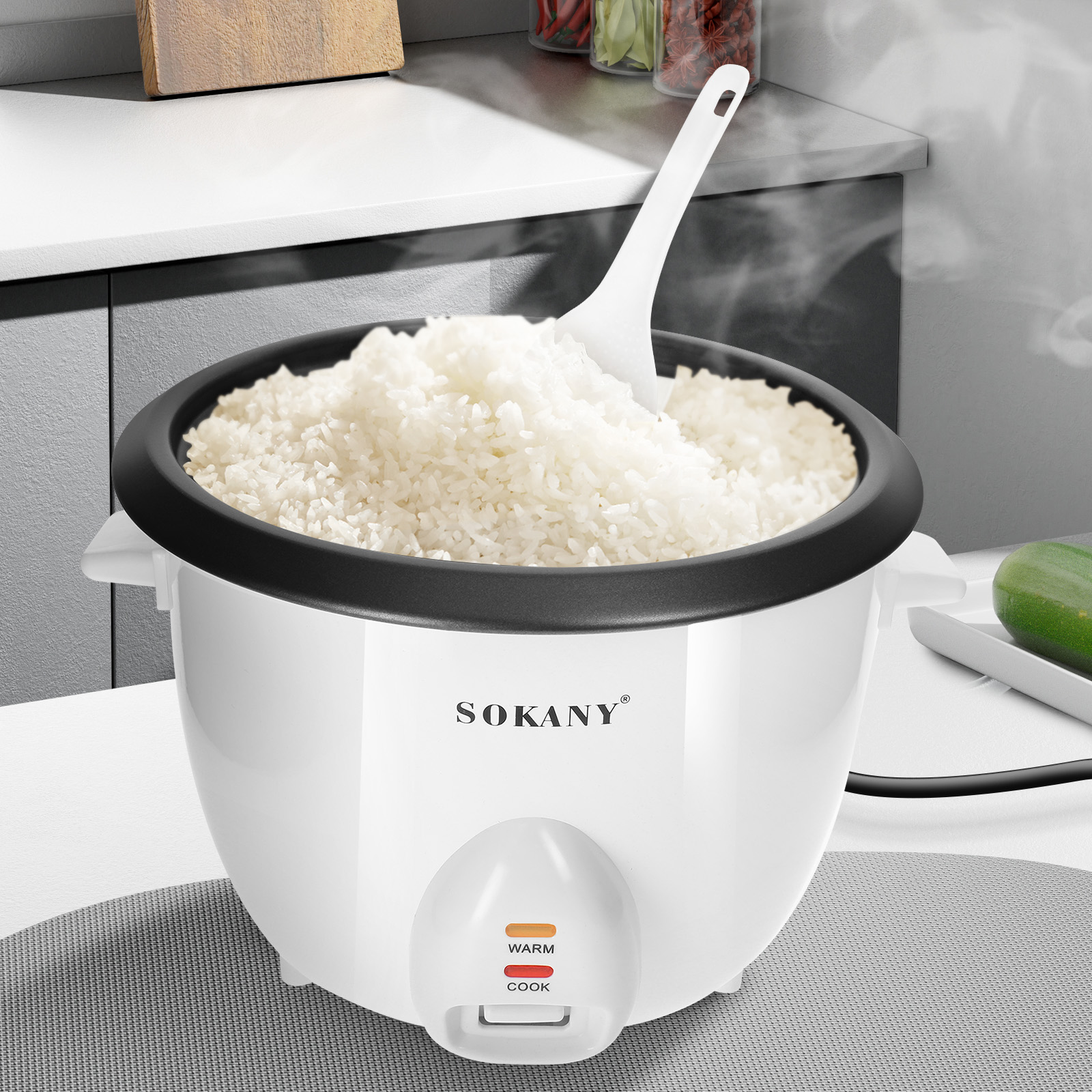 Arrocera blanca con arroz cocido y una cuchara blanca. El vapor sale del arroz. La marca es Sokany.