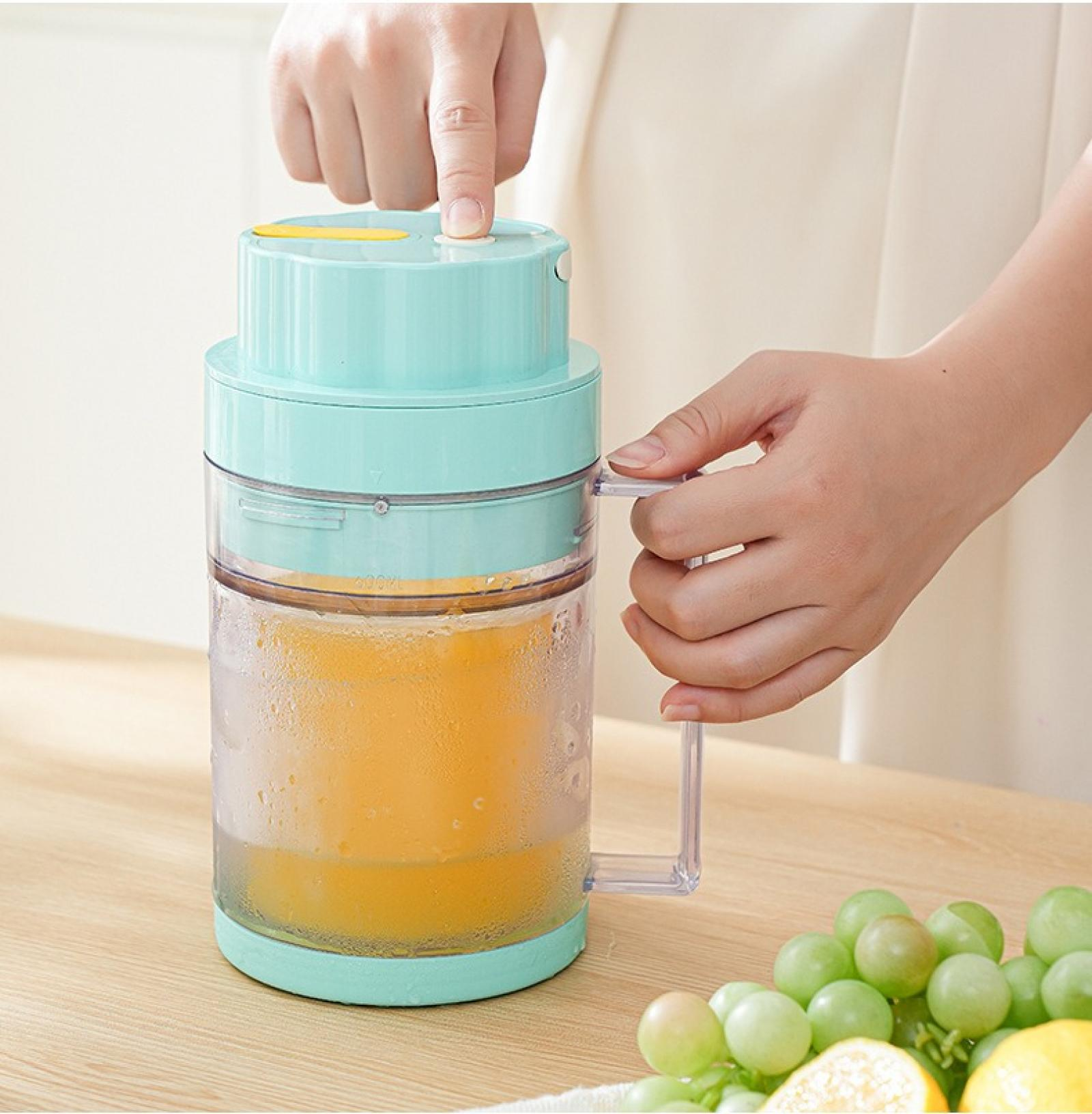 Eine Person drückt einen Knopf auf einem Entsafter. Der Entsafter ist mit Orangensaft gefüllt. Trauben und eine Zitrone liegen auf dem Tisch.